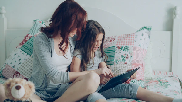 Ibu dan anak perempuan tersenyum gembira belajar bersama menggunakan tablet di rumah