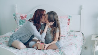 A mother kisses her daughter on the bed.