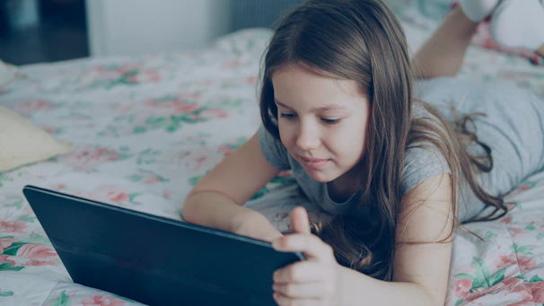 A girl is using a tablet on her bed.