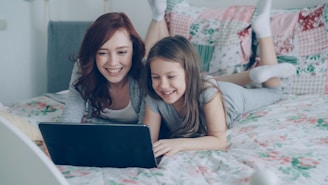Mother and daughter laugh while using a laptop.