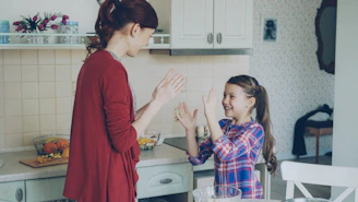 Mother and daughter are playing patty-cake in the kitchen.