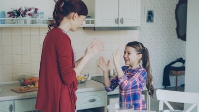 Mother and daughter are playing patty-cake in the kitchen.