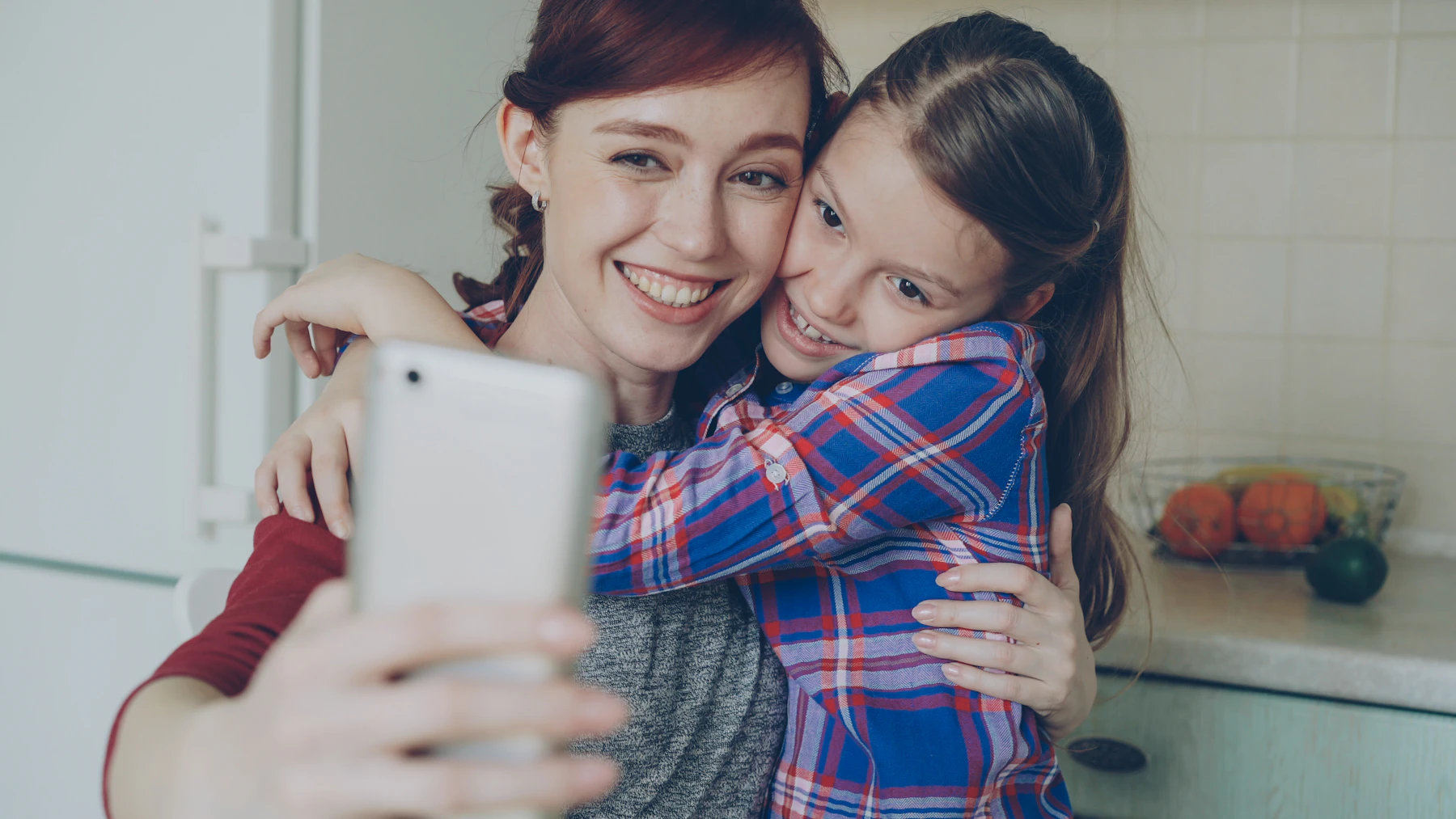 Mãe e filha sorrindo juntas usando o celular em casa