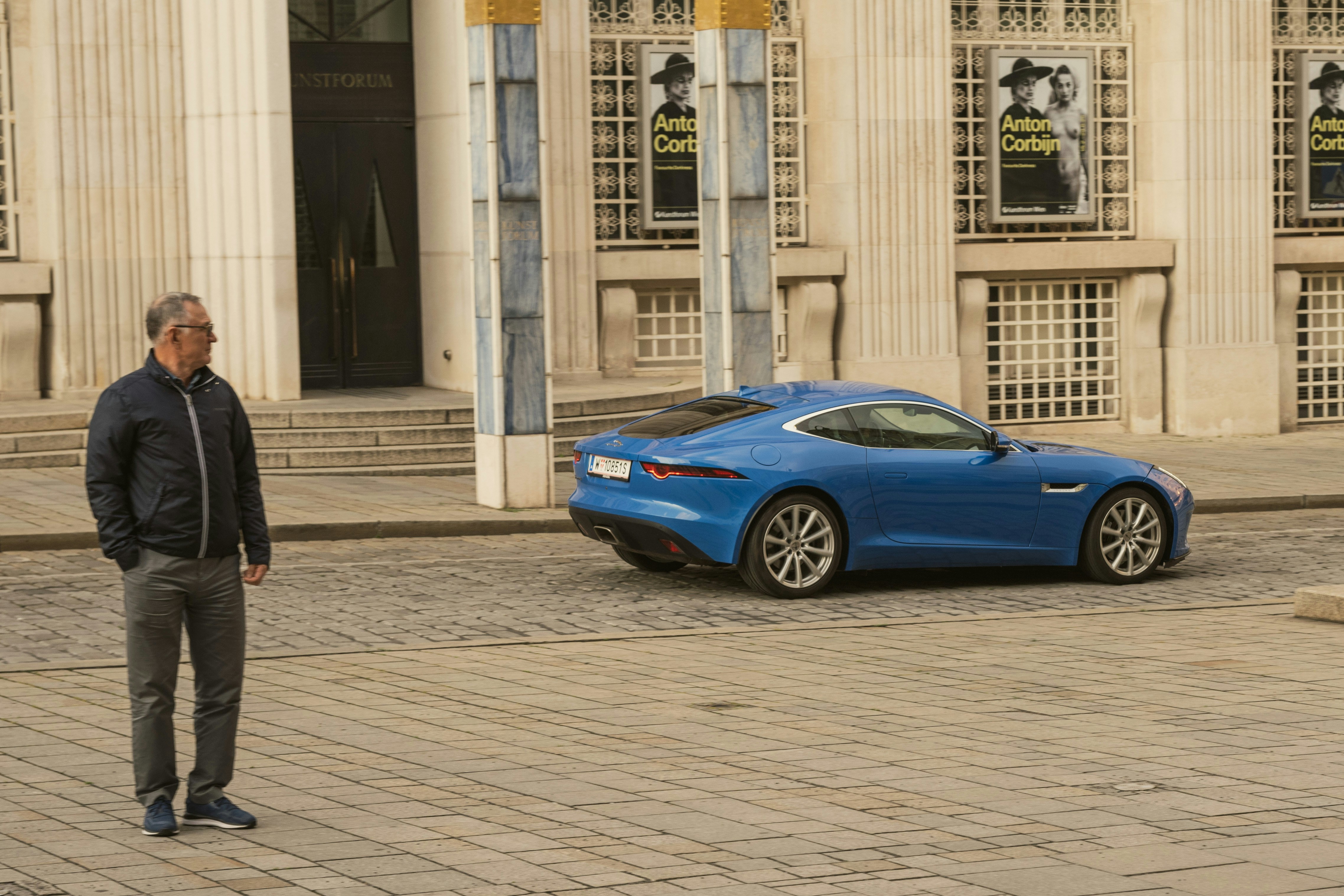 Man stands near a blue sports car outside a building.