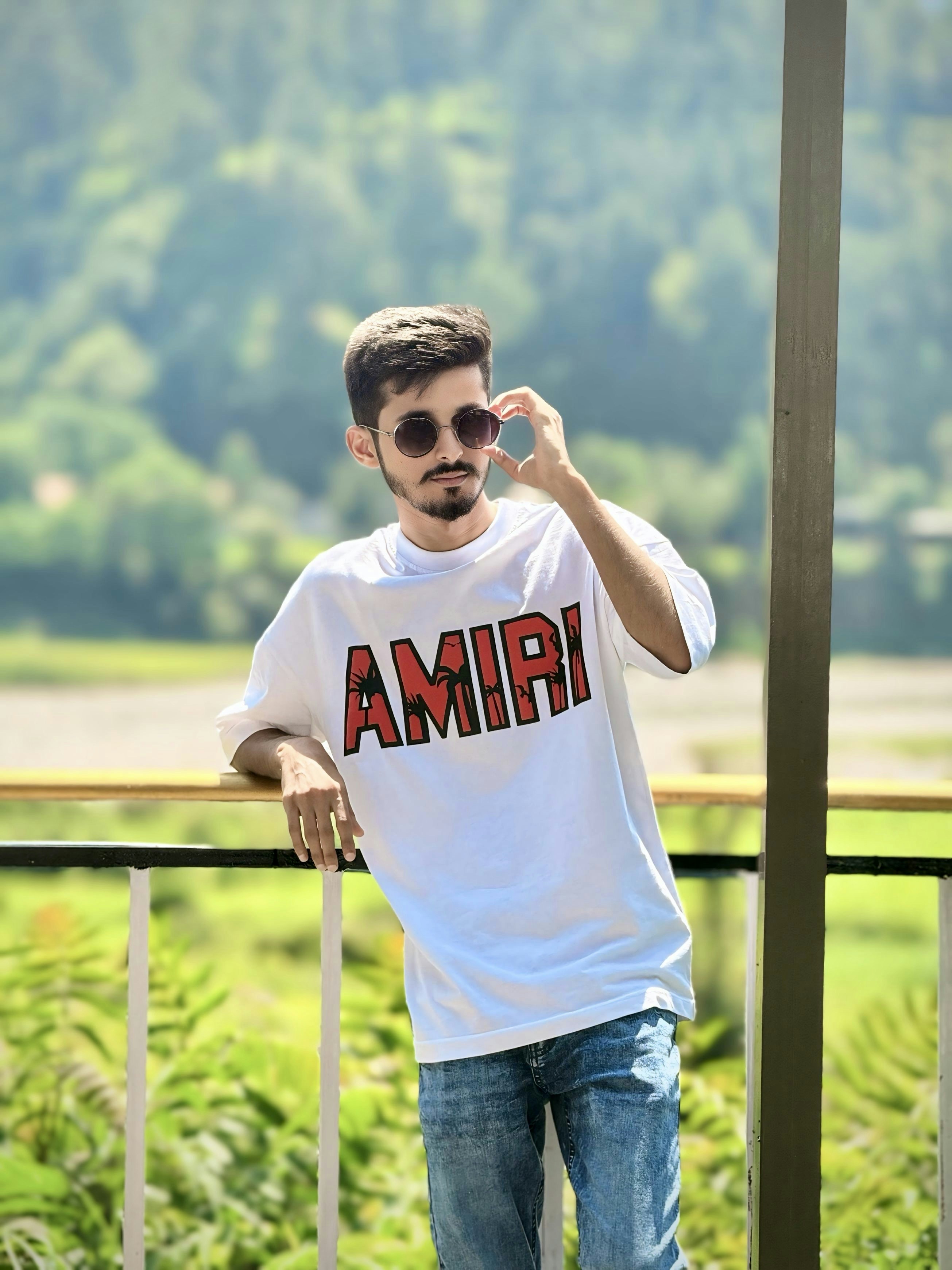 A young man poses with sunglasses and an amiri shirt.