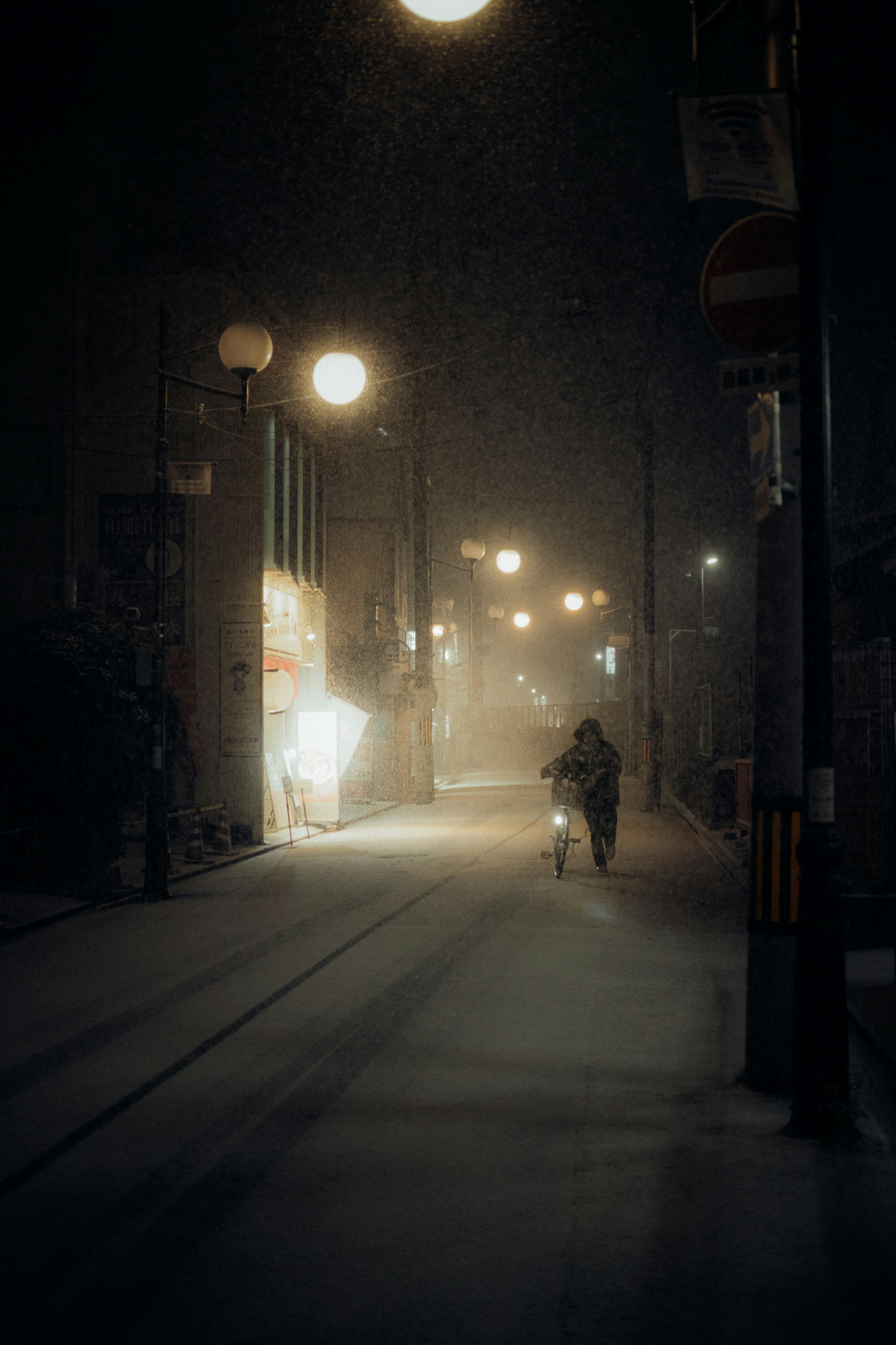 A lone cyclist rides down a snowy street at night.