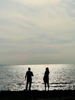 Two silhouetted figures stare at a sparkling ocean.