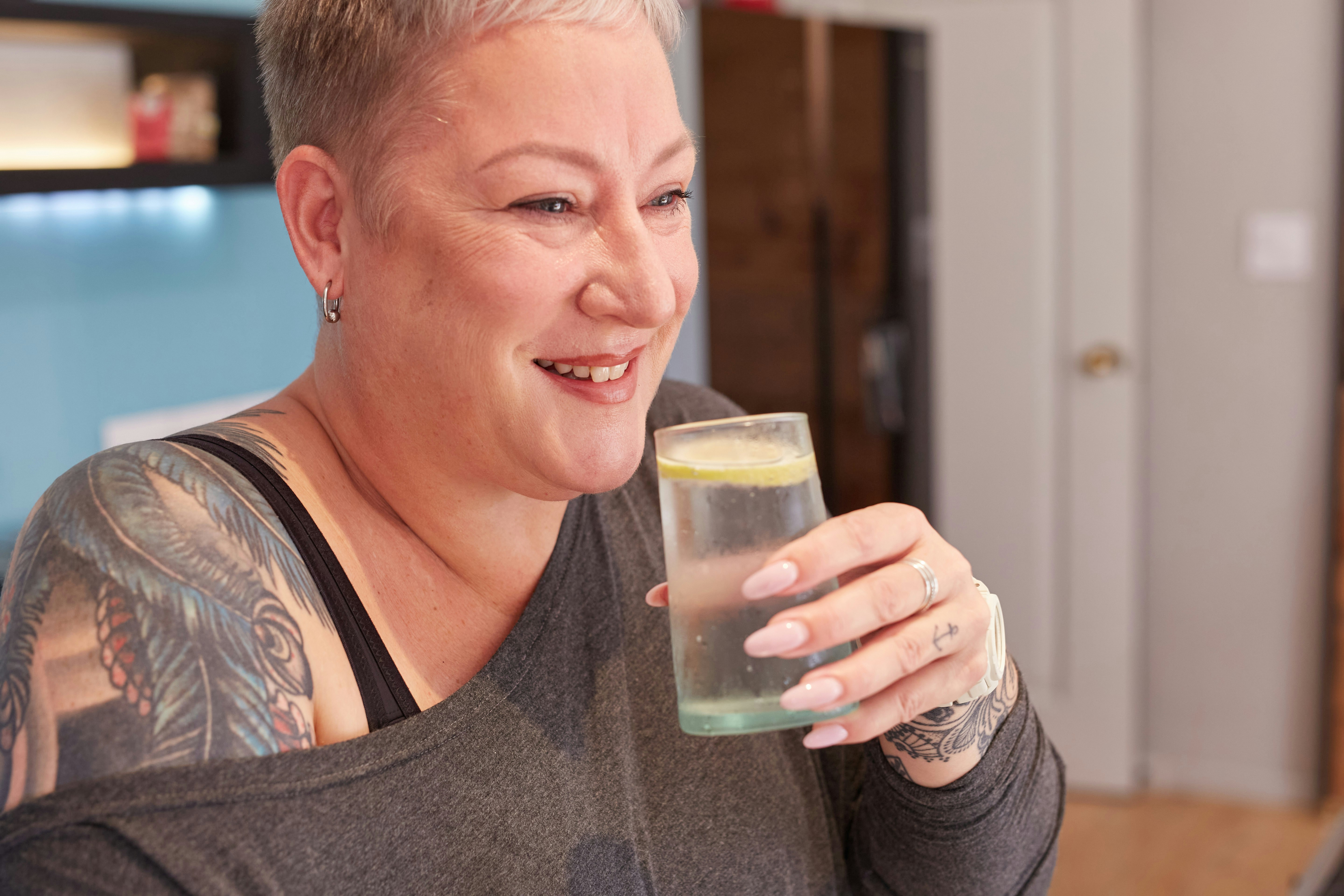A woman smiles while holding a glass of water.