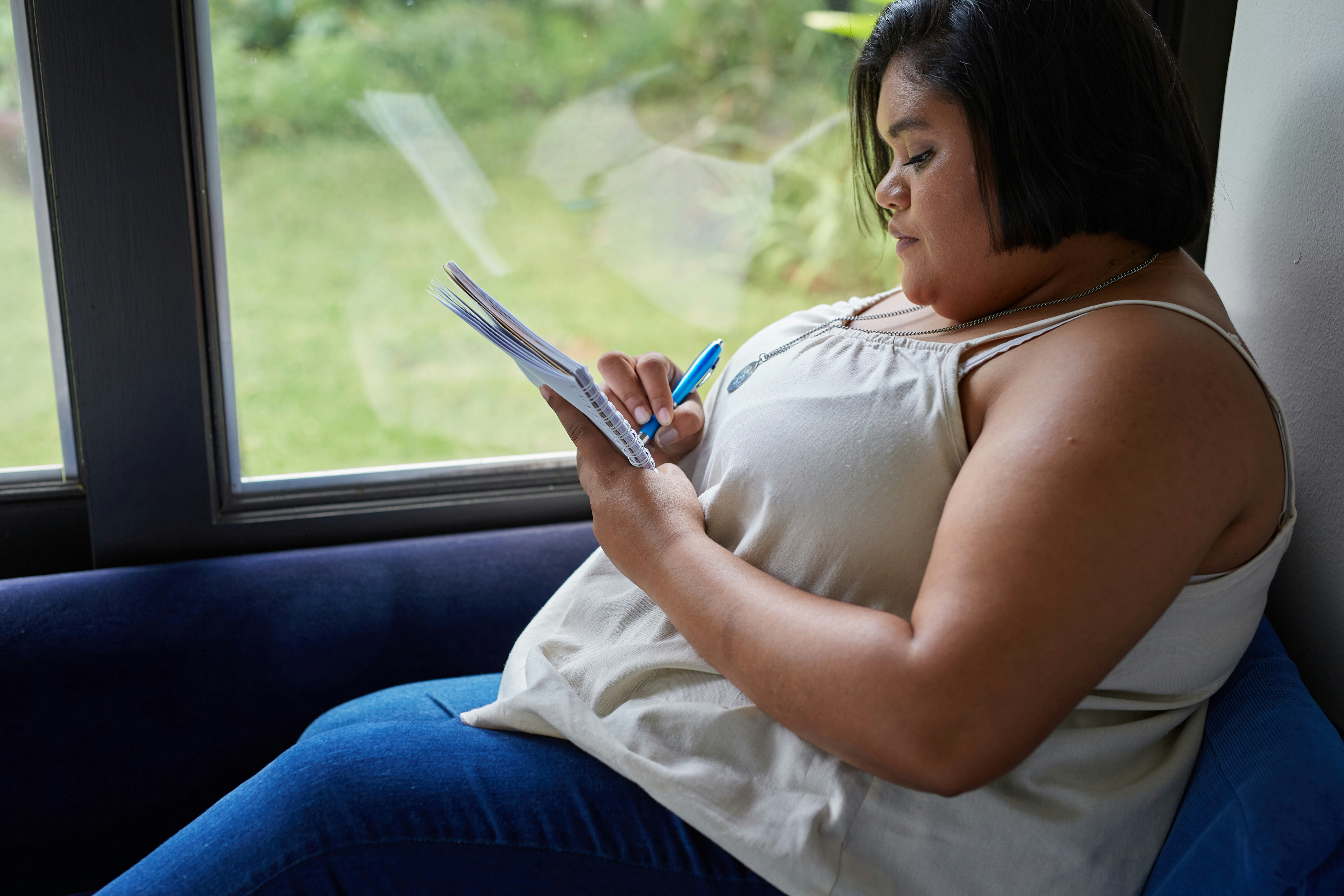Eine Frau schreibt in ein Notizbuch am Fenster.