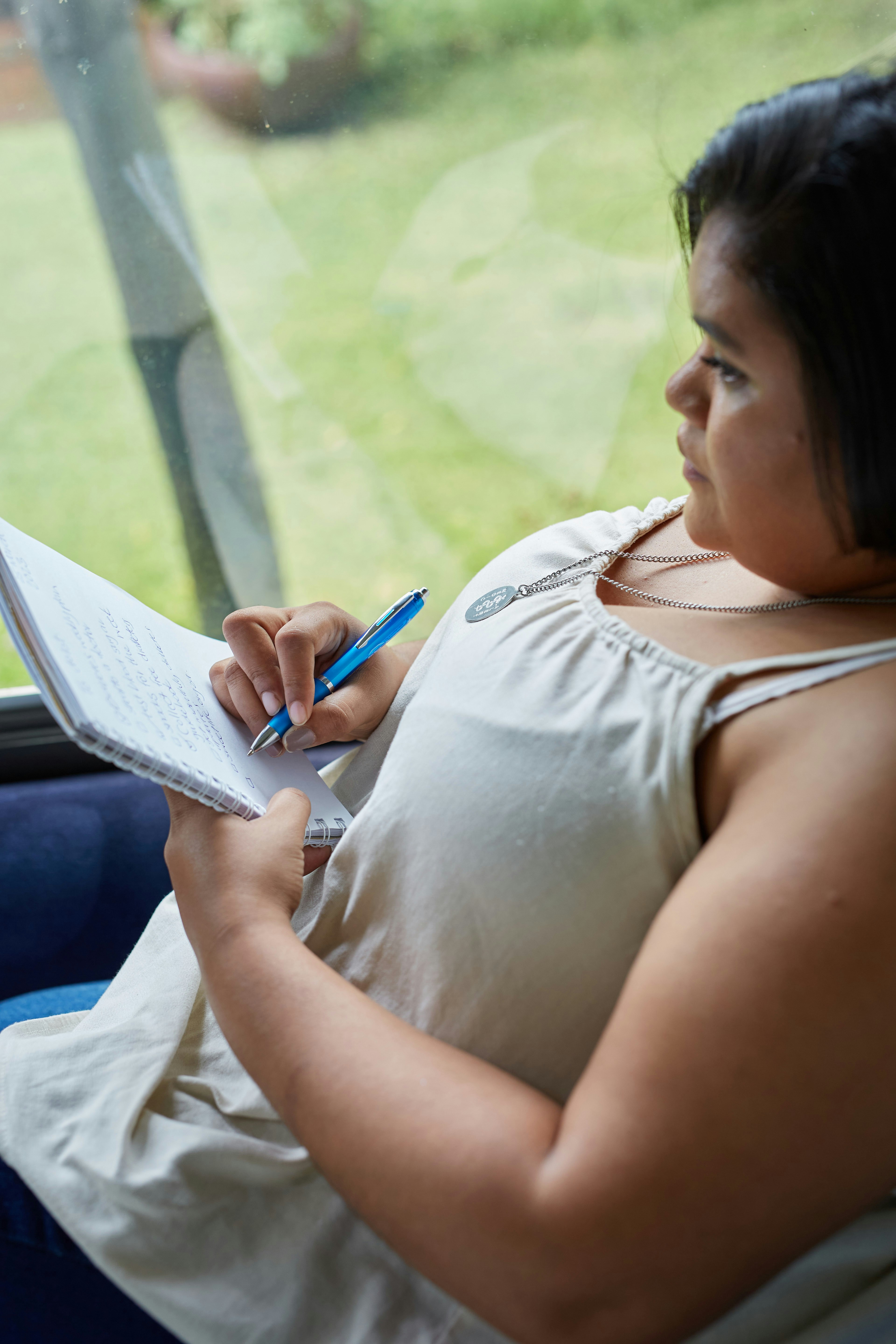 Frau schreibt in ein Notizbuch am Fenster.