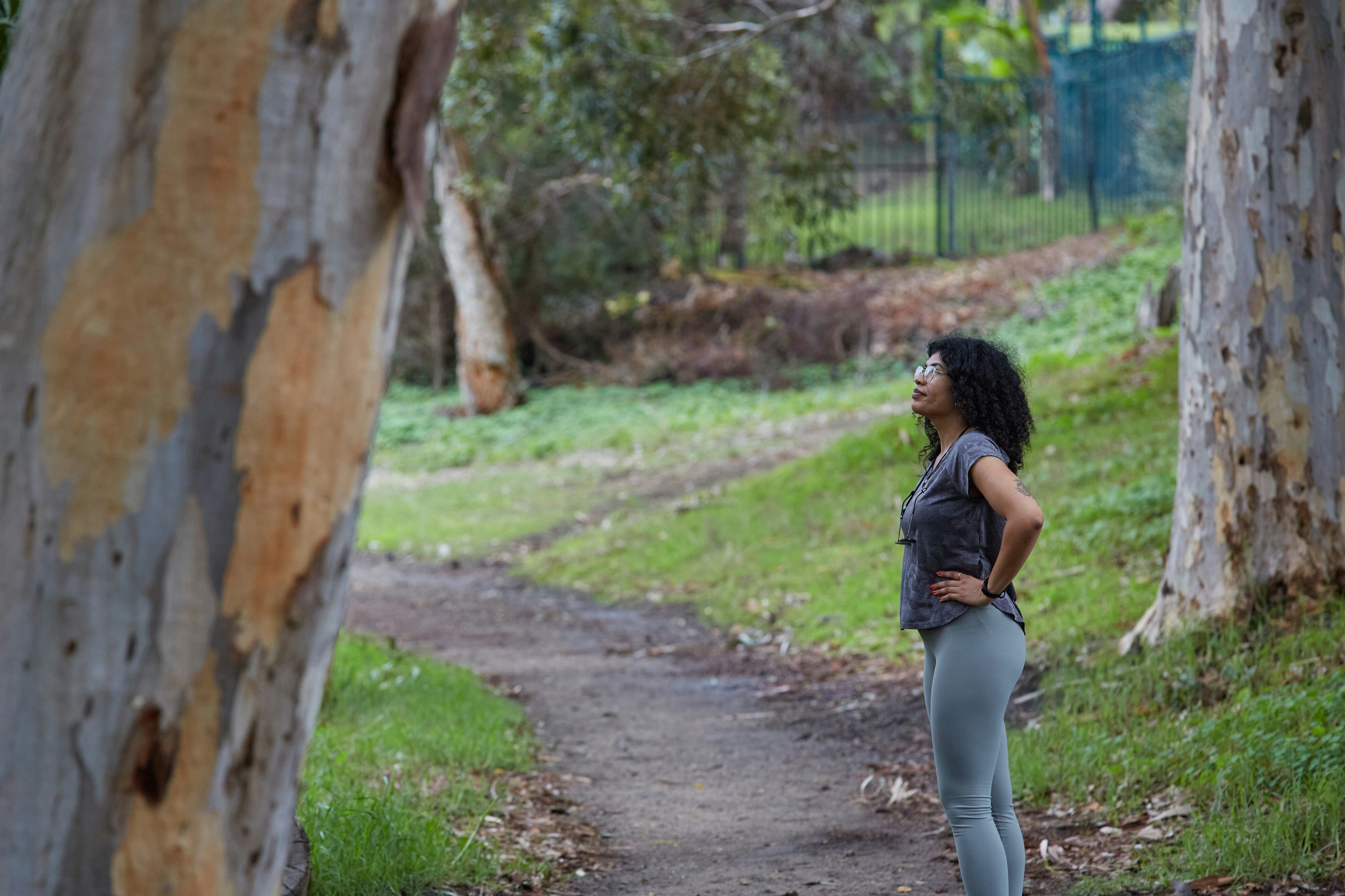 Eine Frau steht auf einem Weg und schaut nach oben zu den Bäumen.