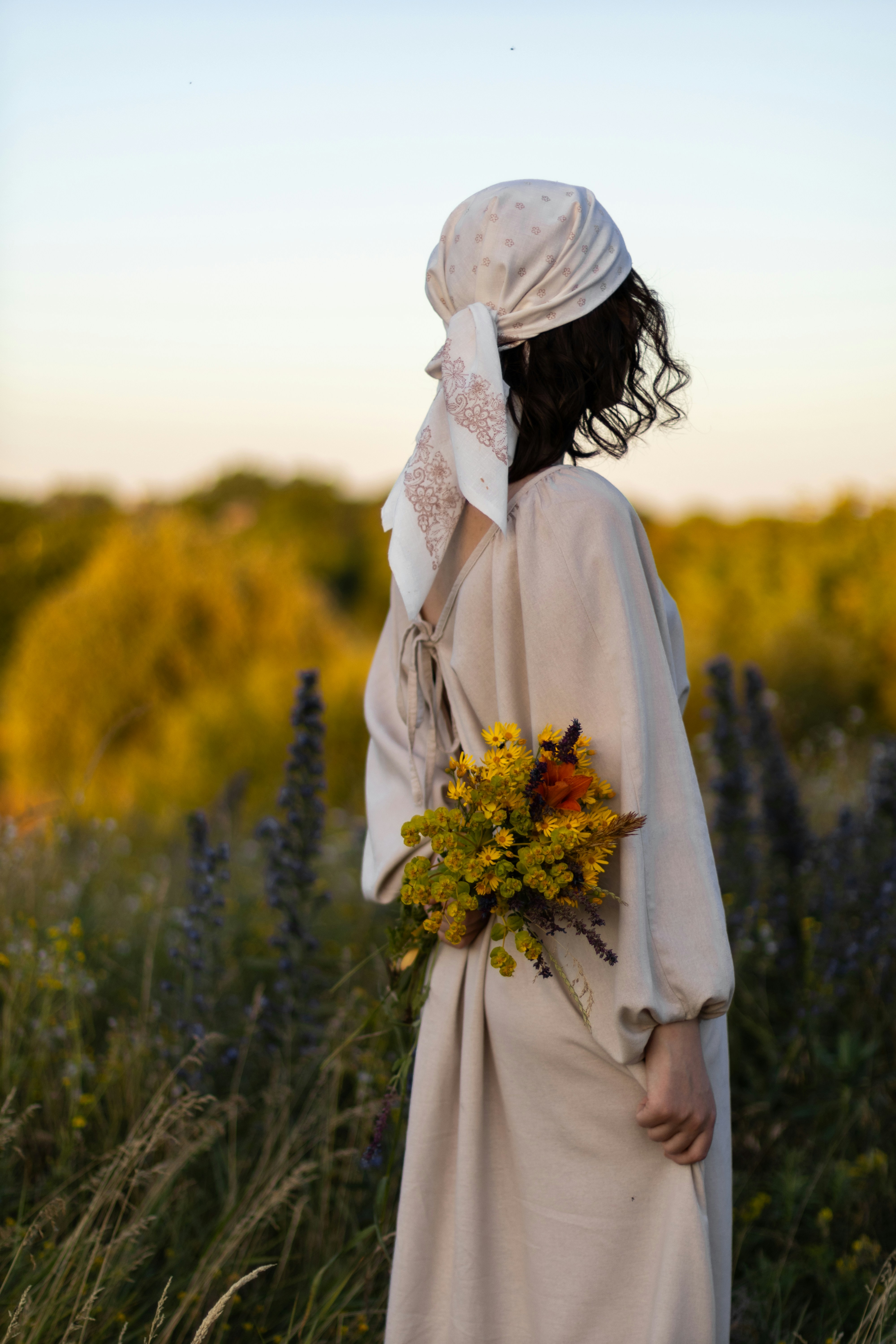 Woman with flowers in field, gazing at the sunset.