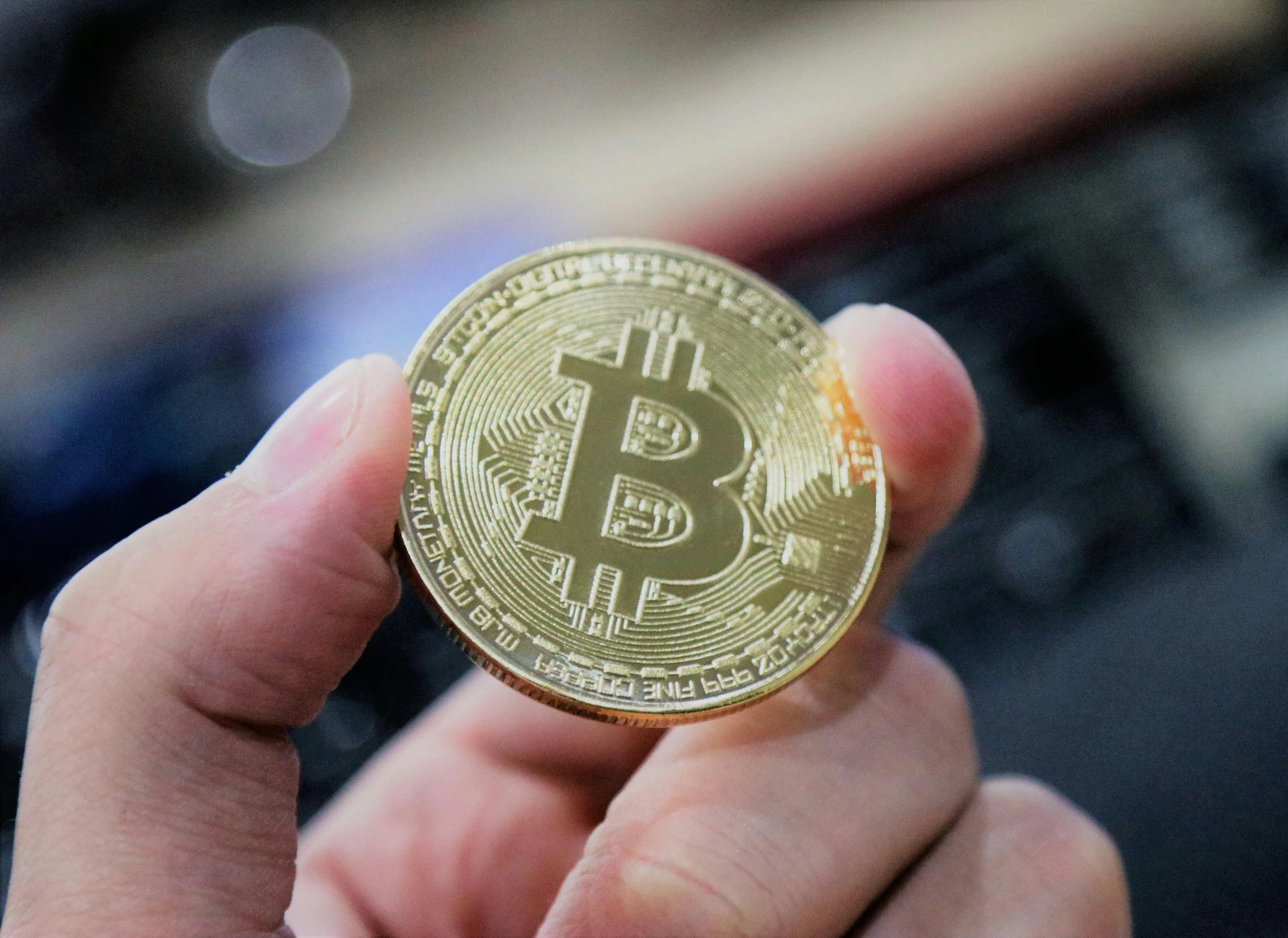 A hand holding a single physical bitcoin token in cool blue light