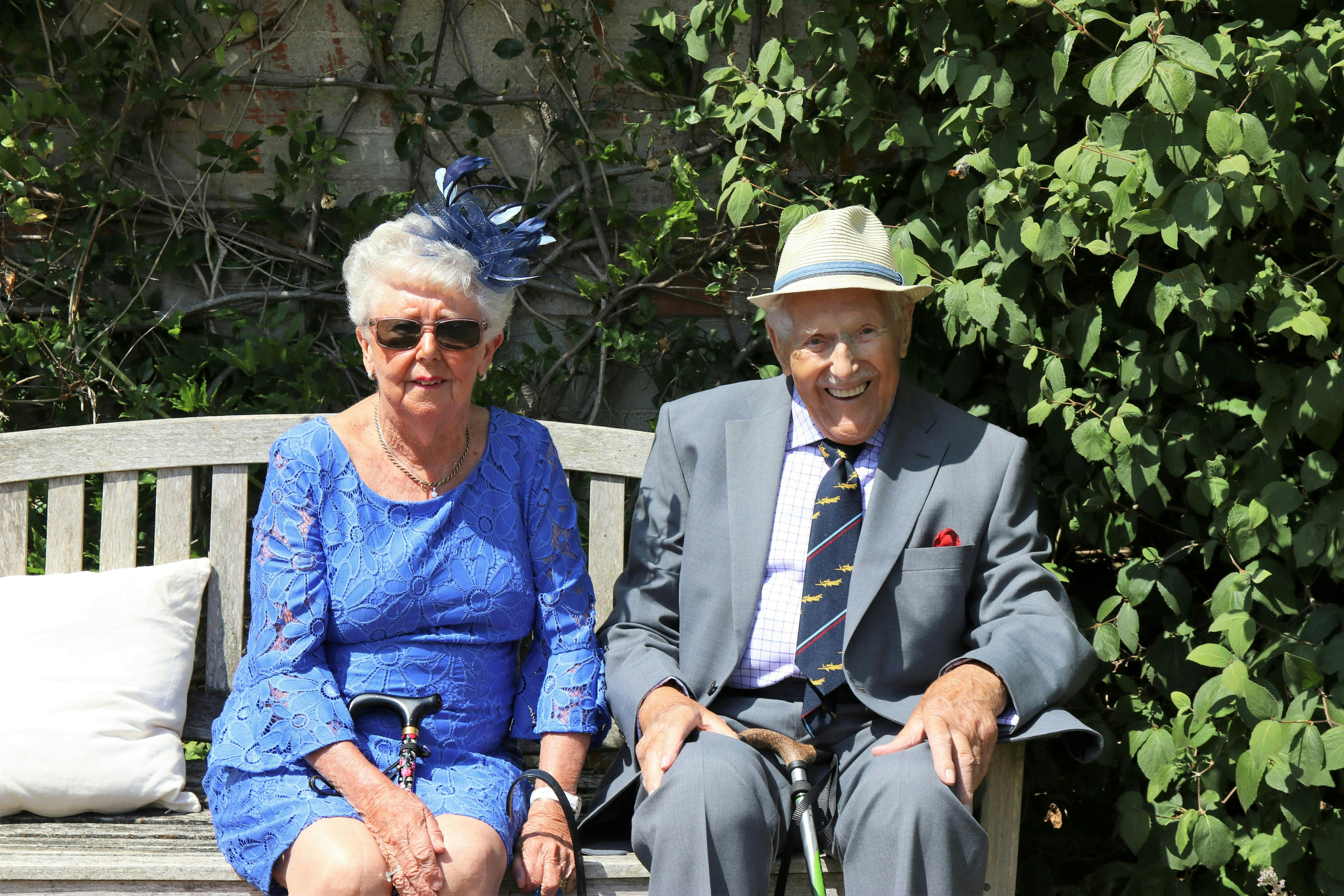 An elderly couple poses on a bench.