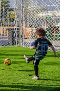 A boy kicks a soccer ball on a green field.