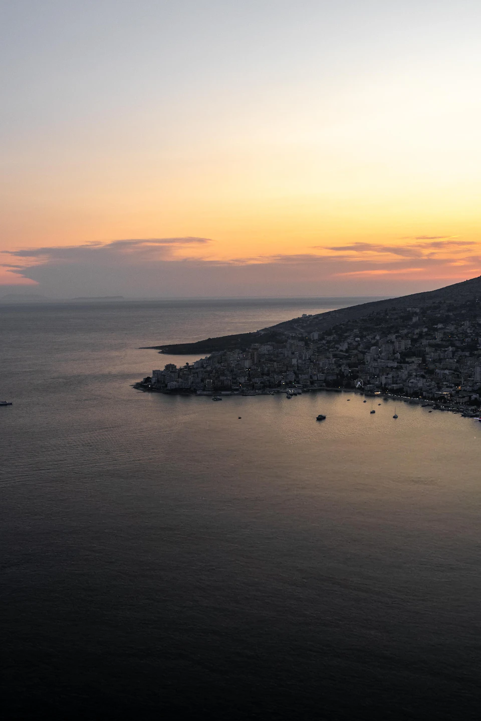 Serene coastal scene at sunset with orange-pink sky, dark blue ocean, and scattered boats