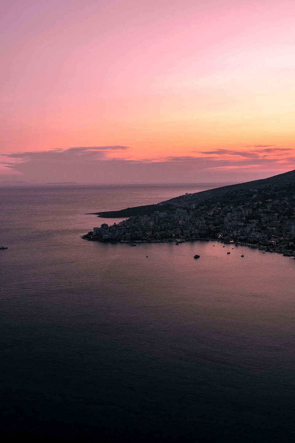 Sunset over ocean with pink and orange hues against dark blue waters and distant hills