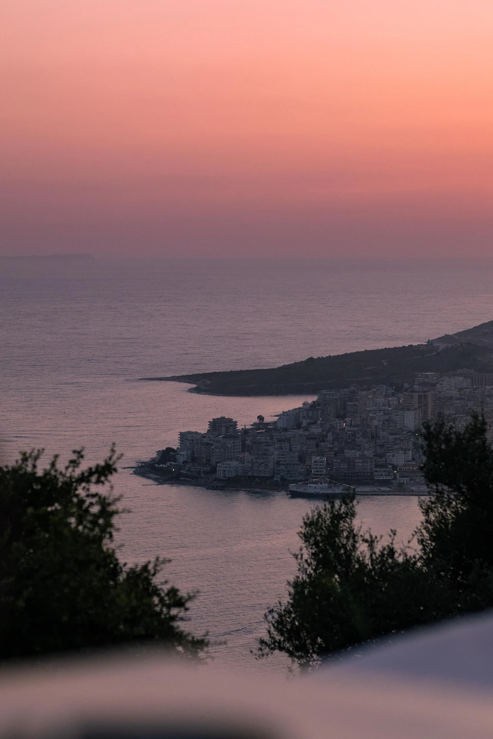 Serene coastal scene at sunset with cityscape and ocean in background, silhouetted buildings