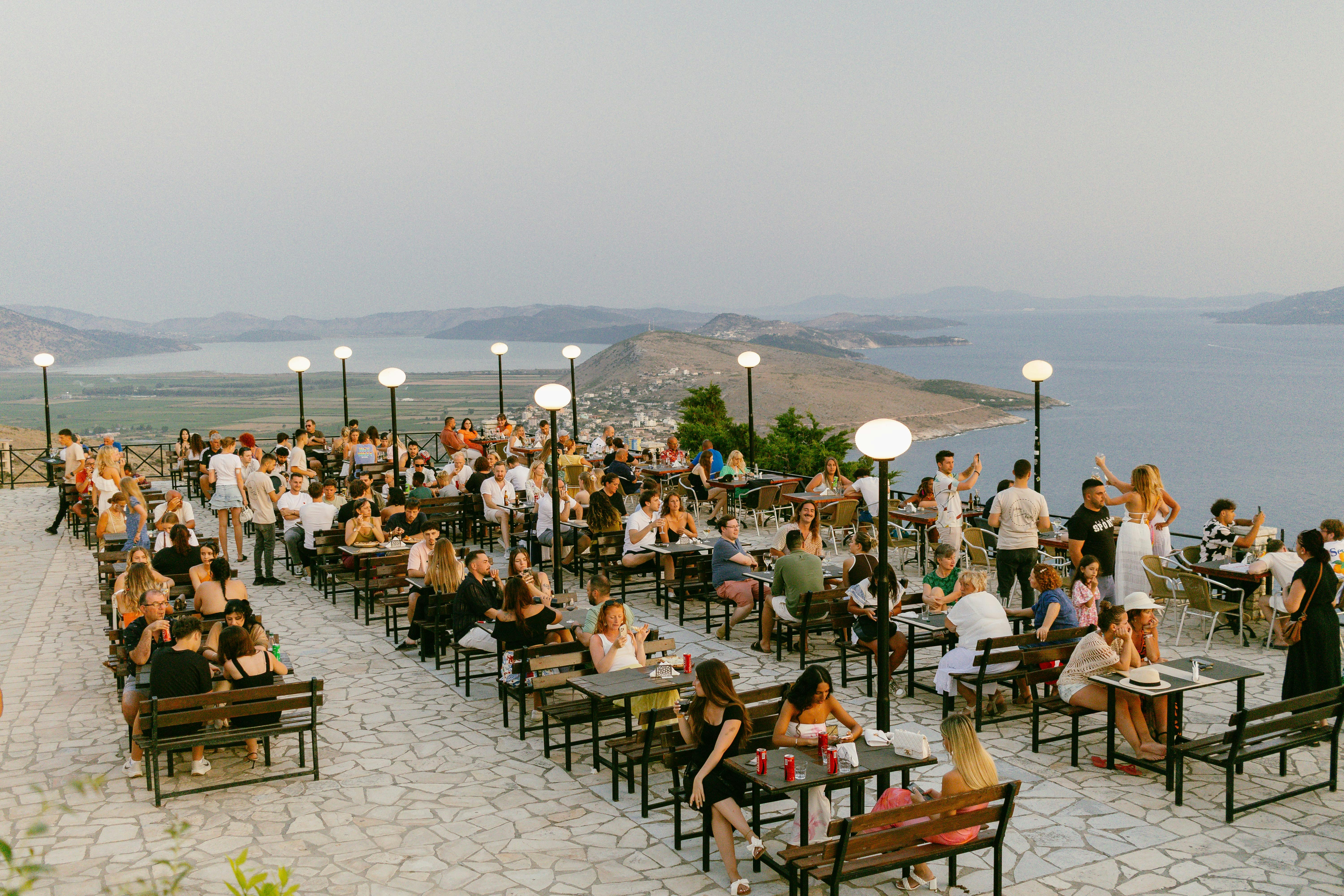 People dine outdoors, overlooking a scenic landscape.