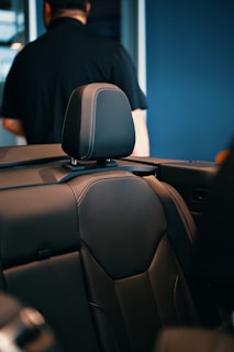 A black car seat with a person in the background.