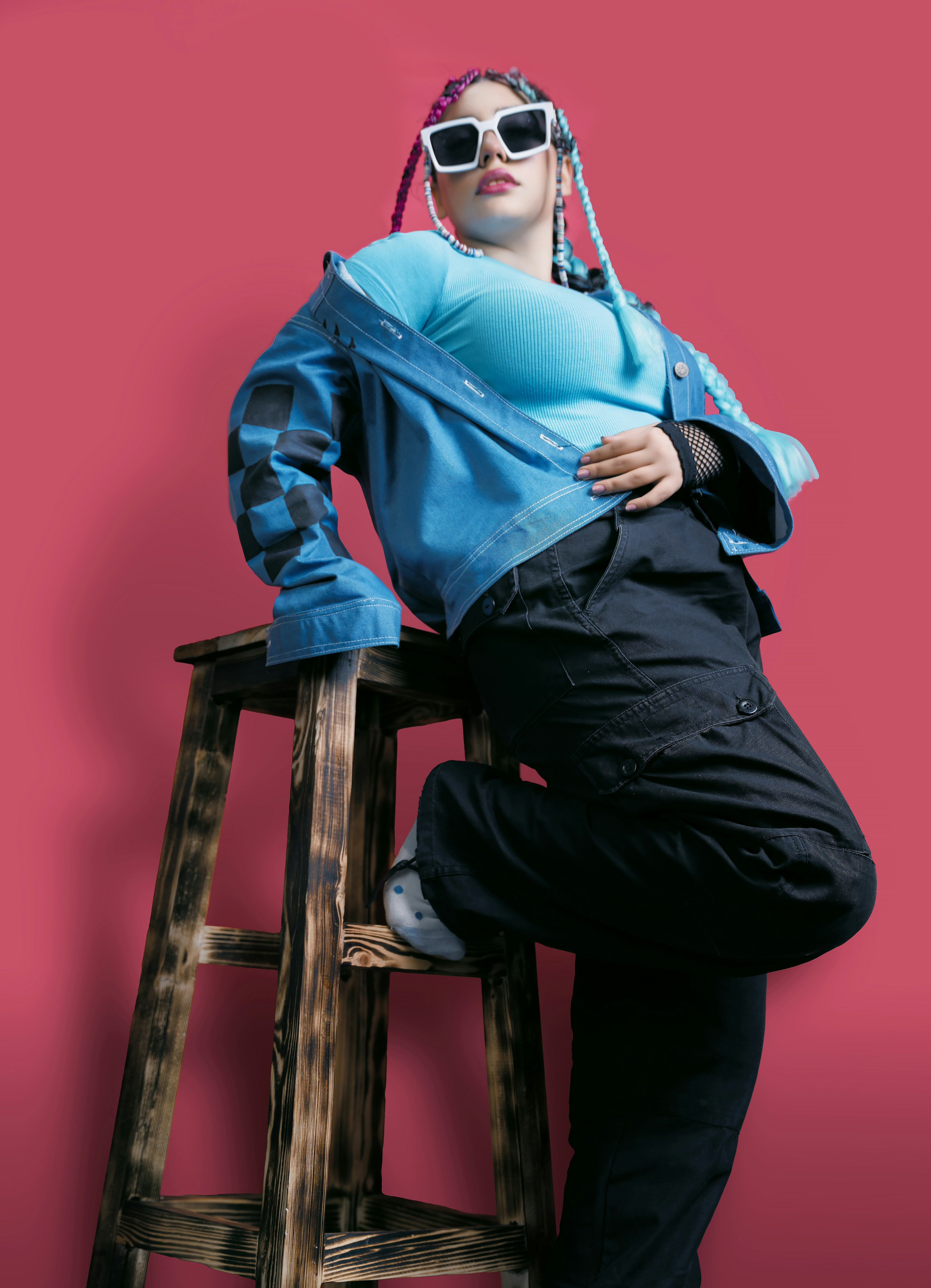 A stylish person poses on a wooden stool.