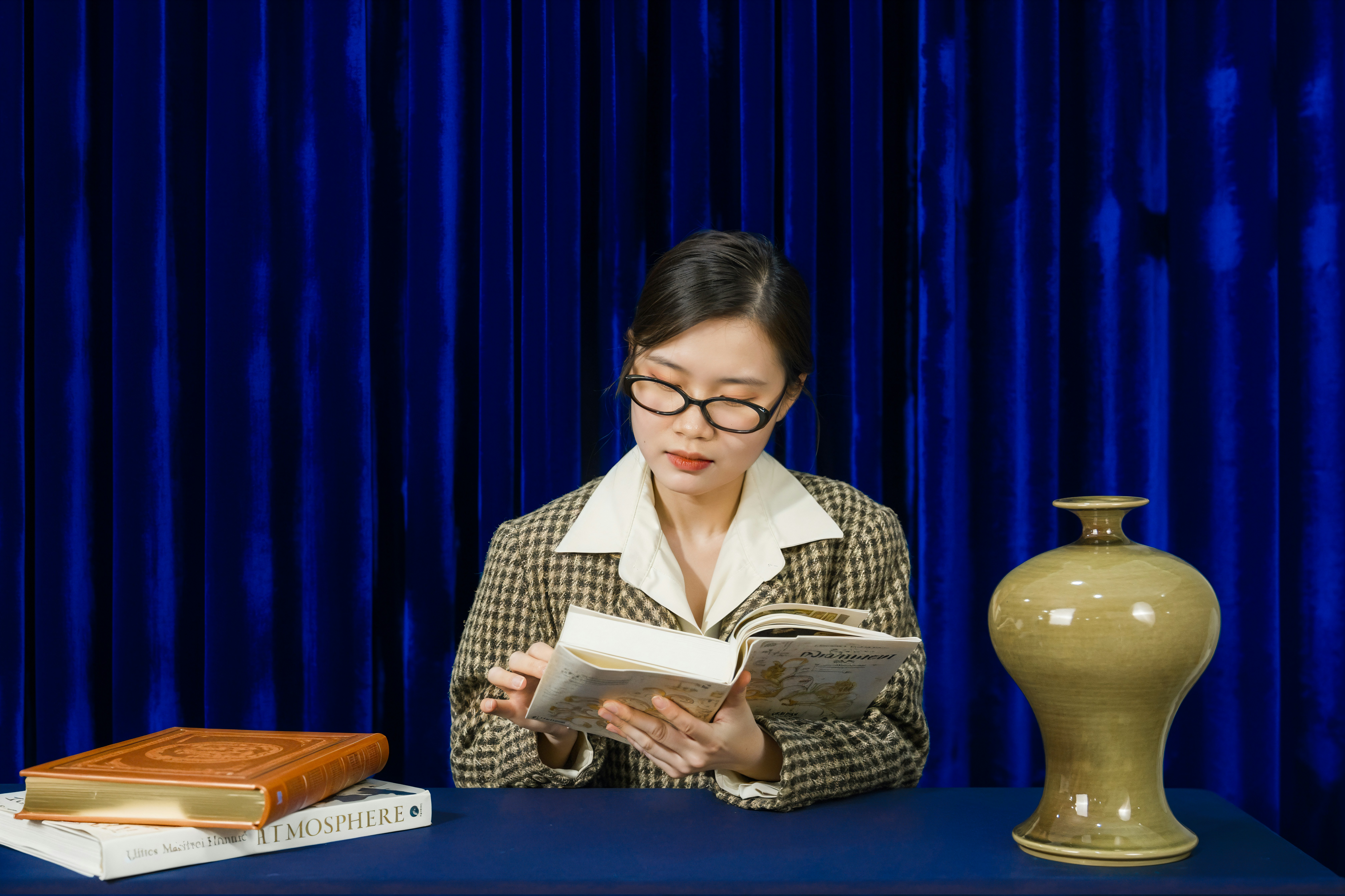 Woman in glasses reading a book at a table.