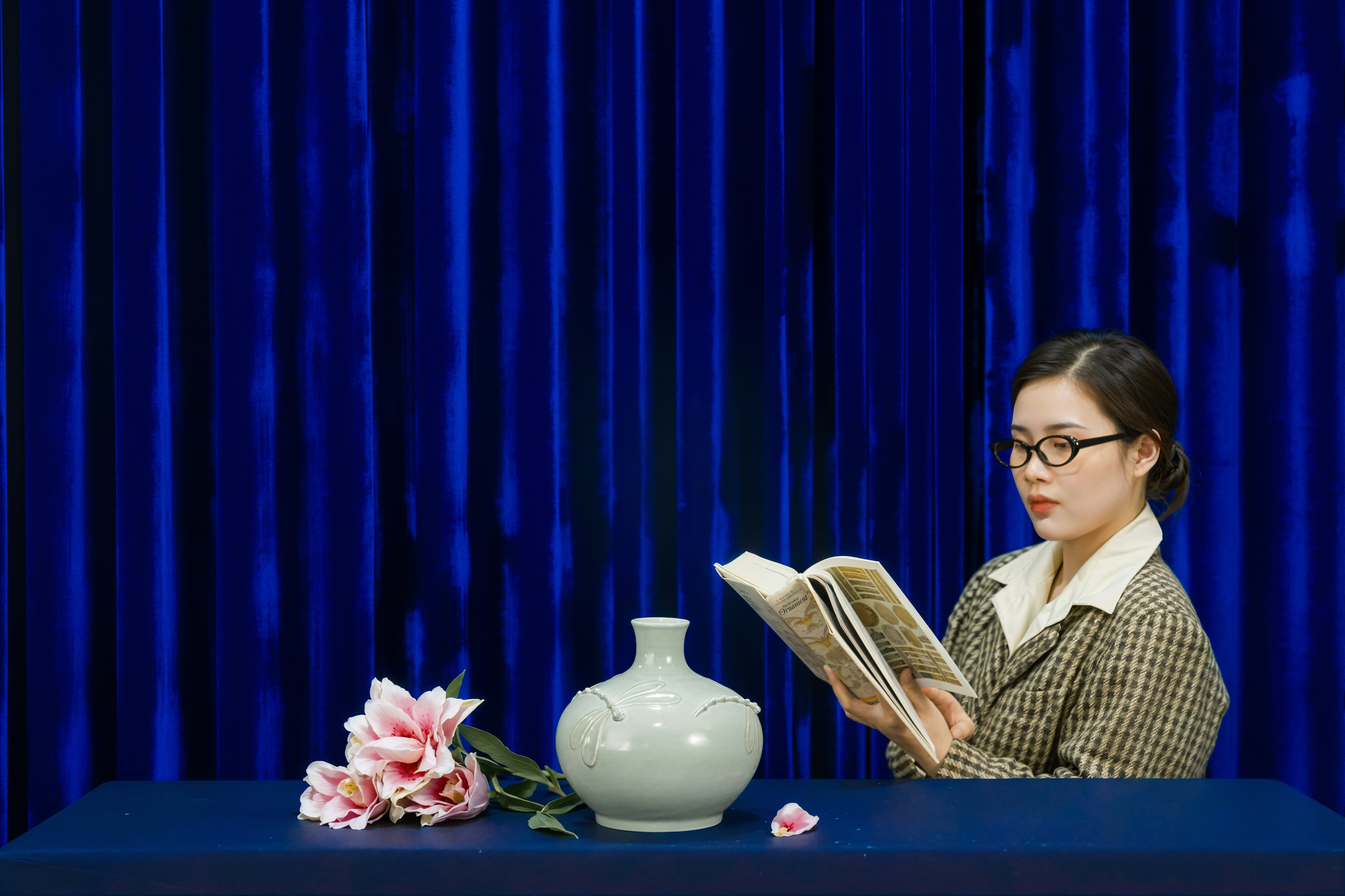 Woman reading a book next to a vase and flowers.