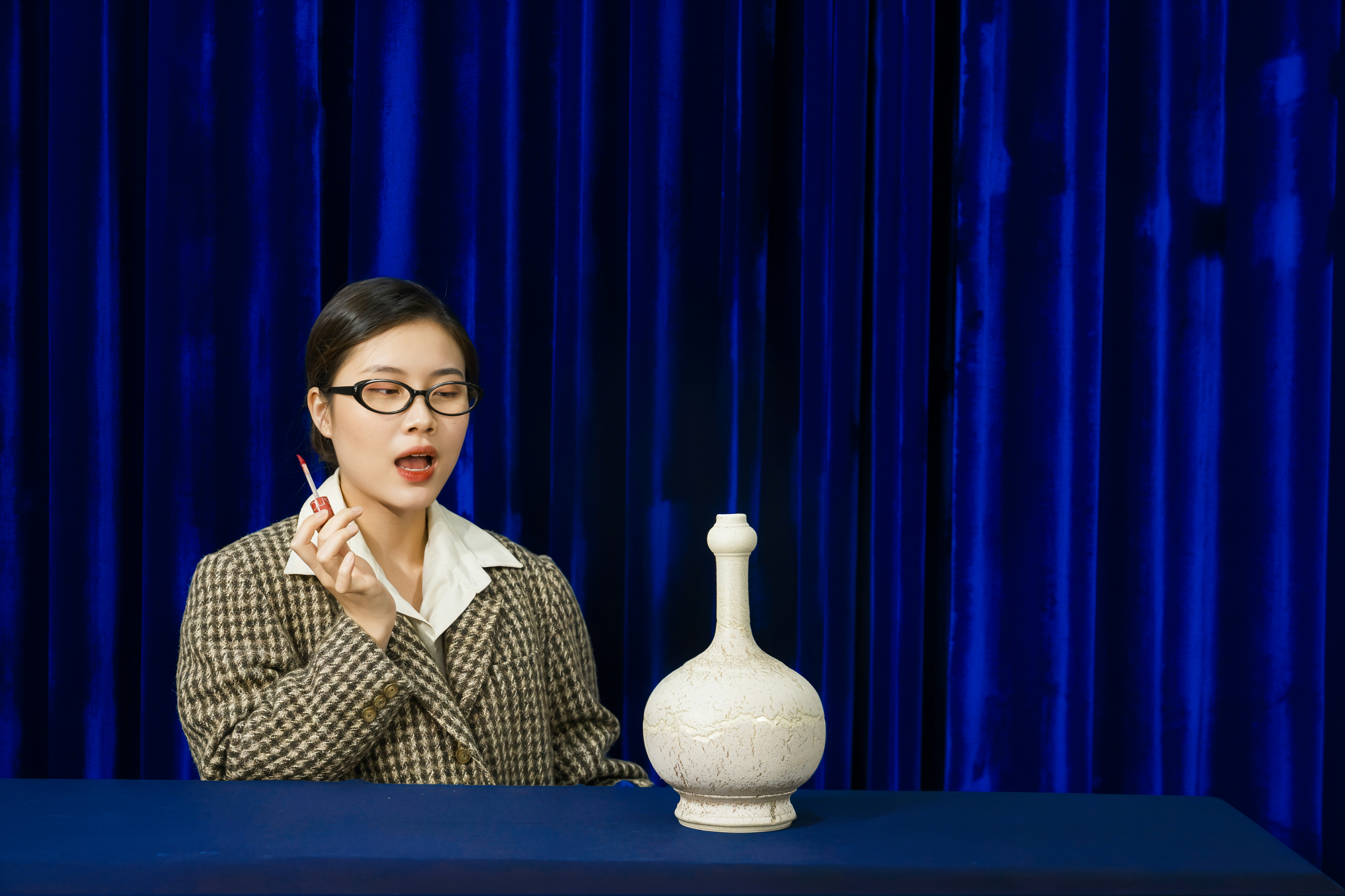 Woman in glasses holds a pen near a vase