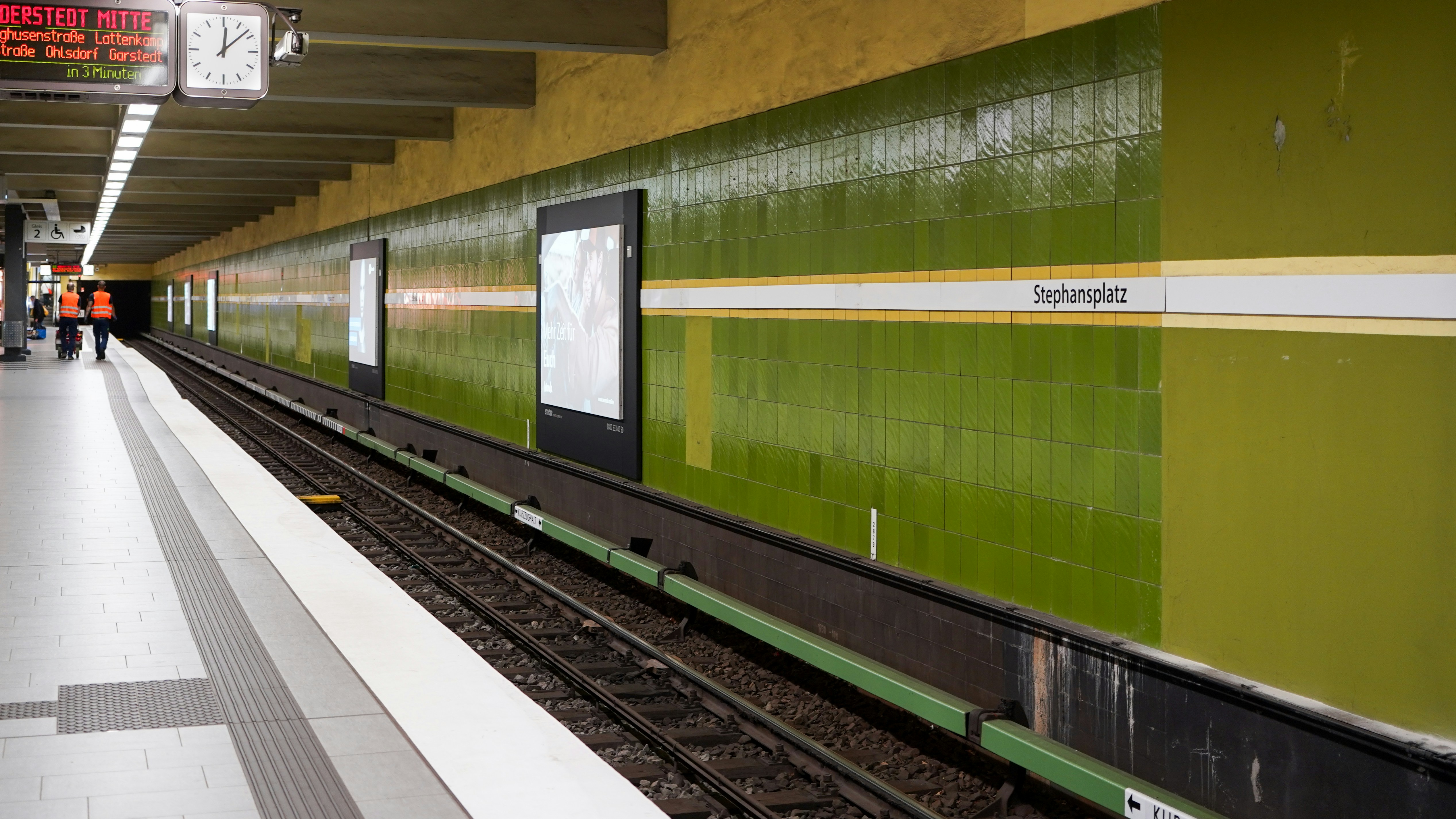 A subway platform with tracks and green walls.