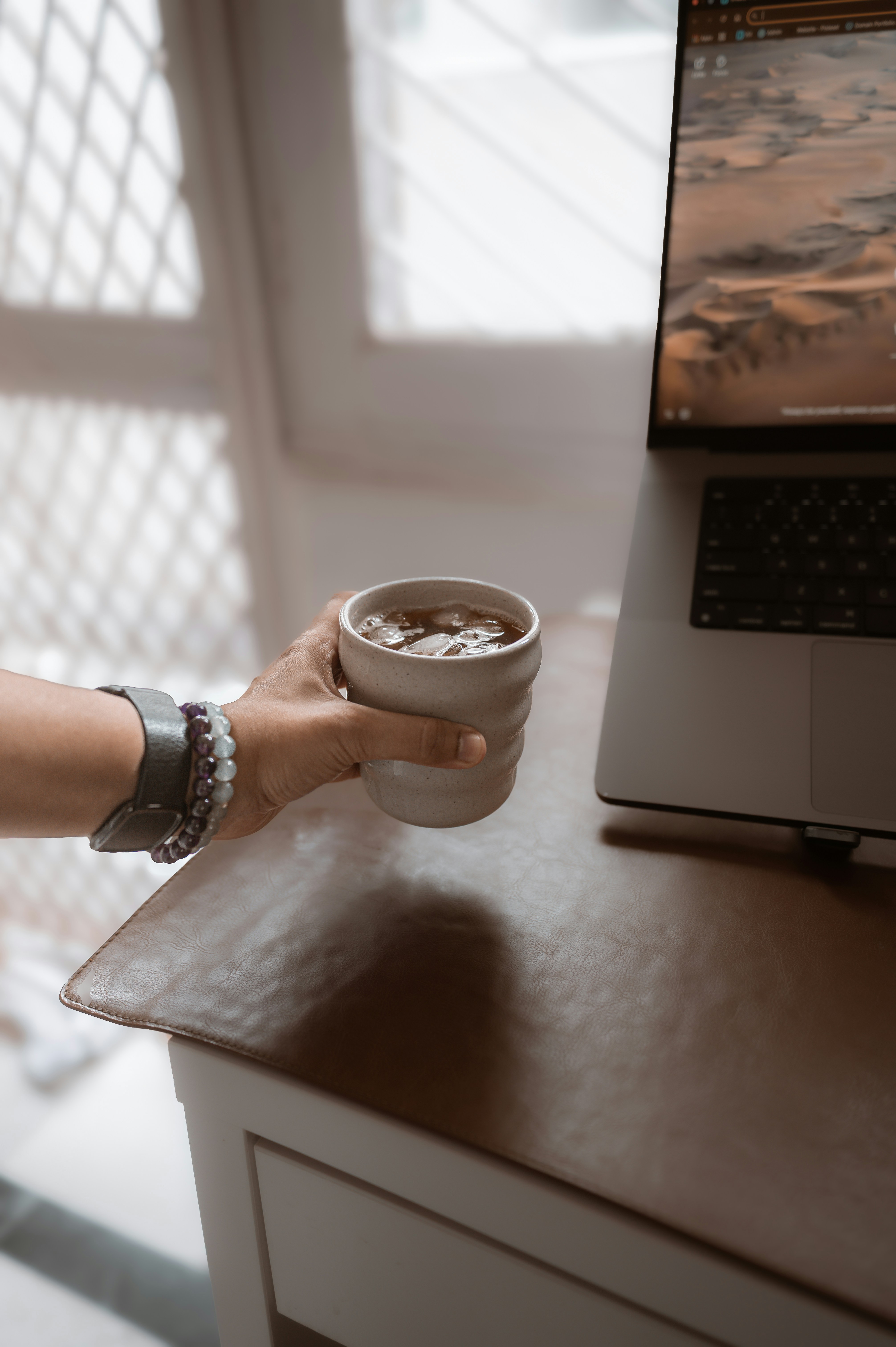 Die Hand hält eine Tasse in der Nähe eines Laptops auf einem Schreibtisch.