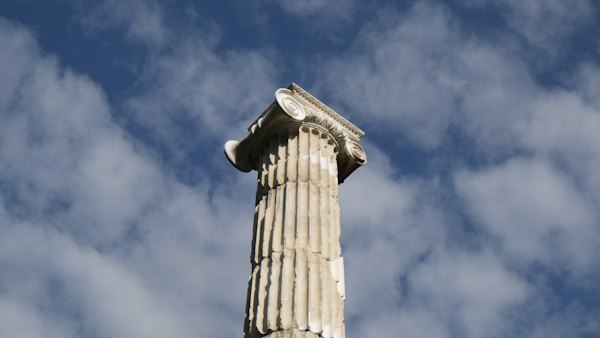 A classic column stands tall against a cloudy sky — Olympia, Greece