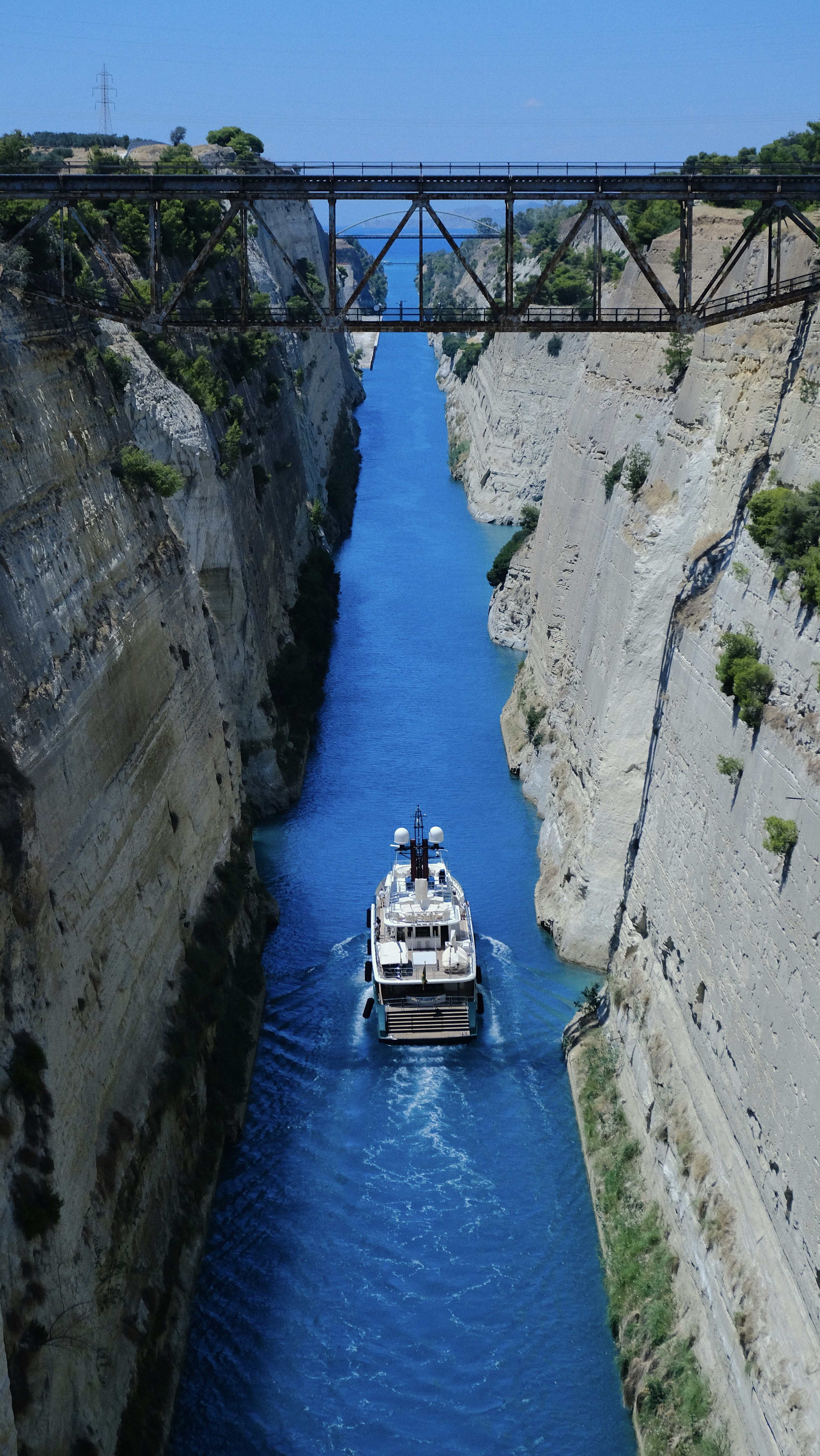 A yacht sails through a canal under a bridge.