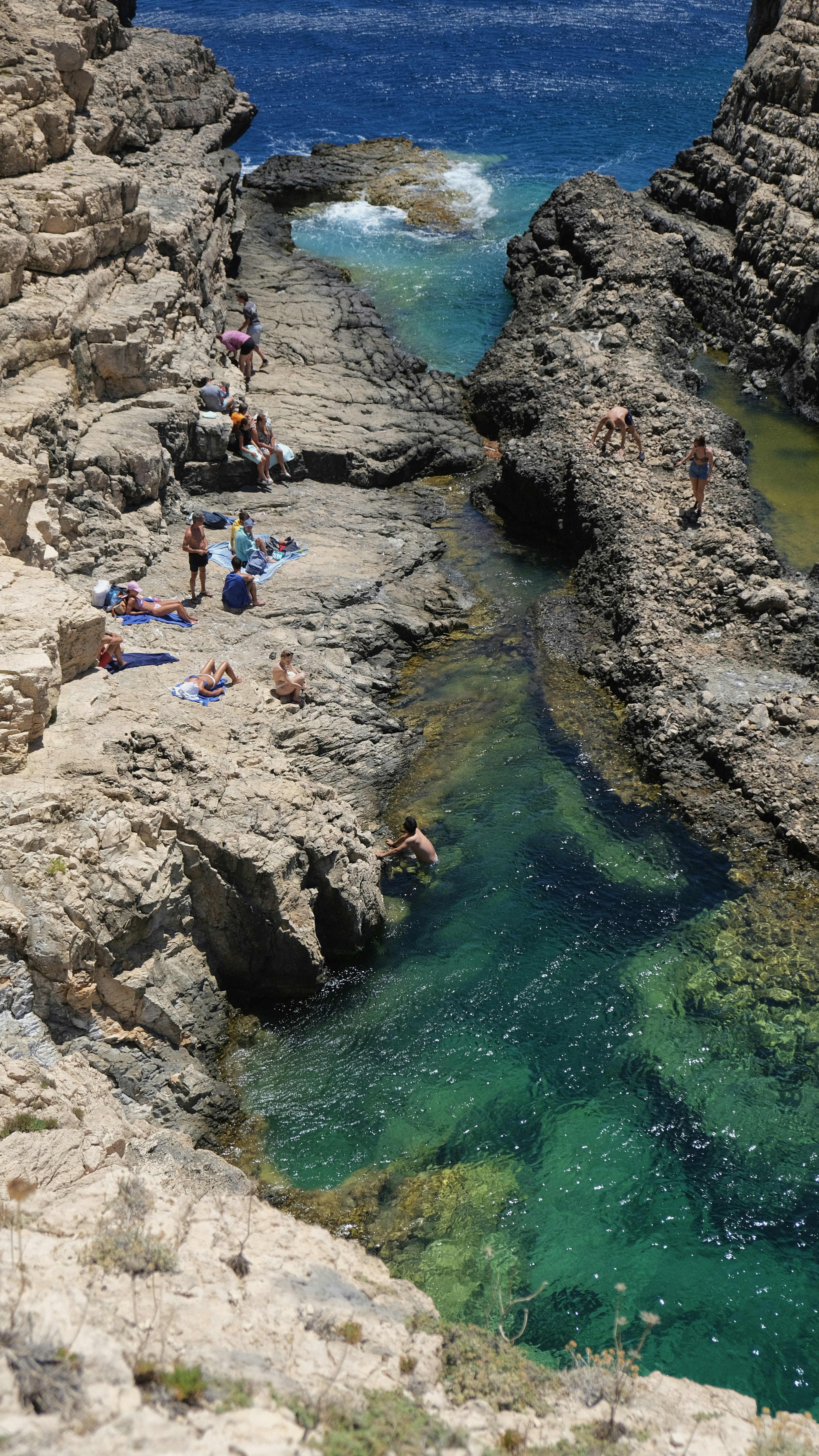 People sunbathe and swim in a beautiful coastal cove.