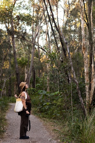 Woman walks along a path, looking up at trees.