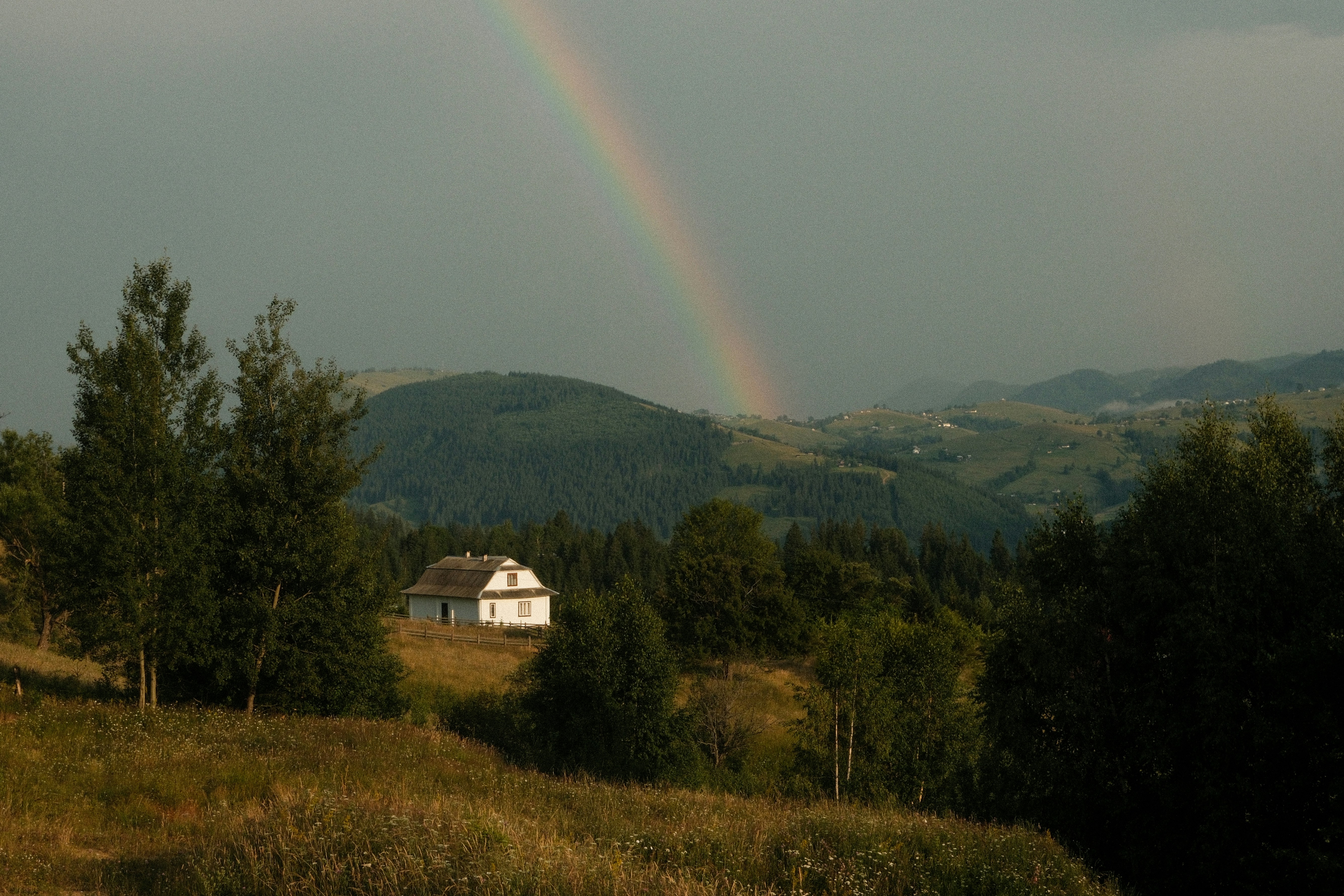 A rainbow arcs over a house in a valley.