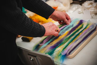 A person is crafting with colorful wool fibers.