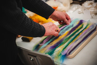 A person is crafting with colorful wool fibers.