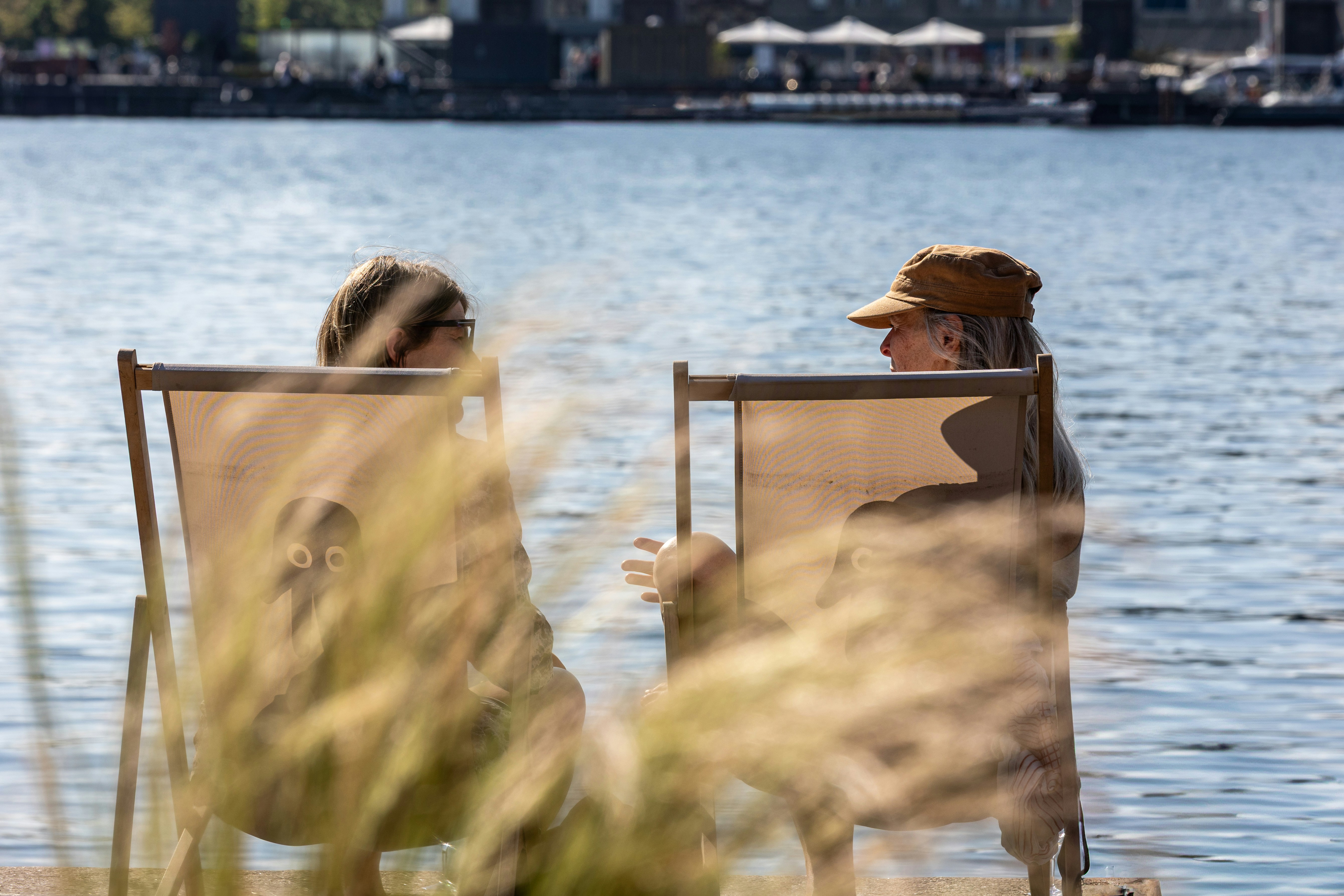 Two people are relaxing in chairs by the water.