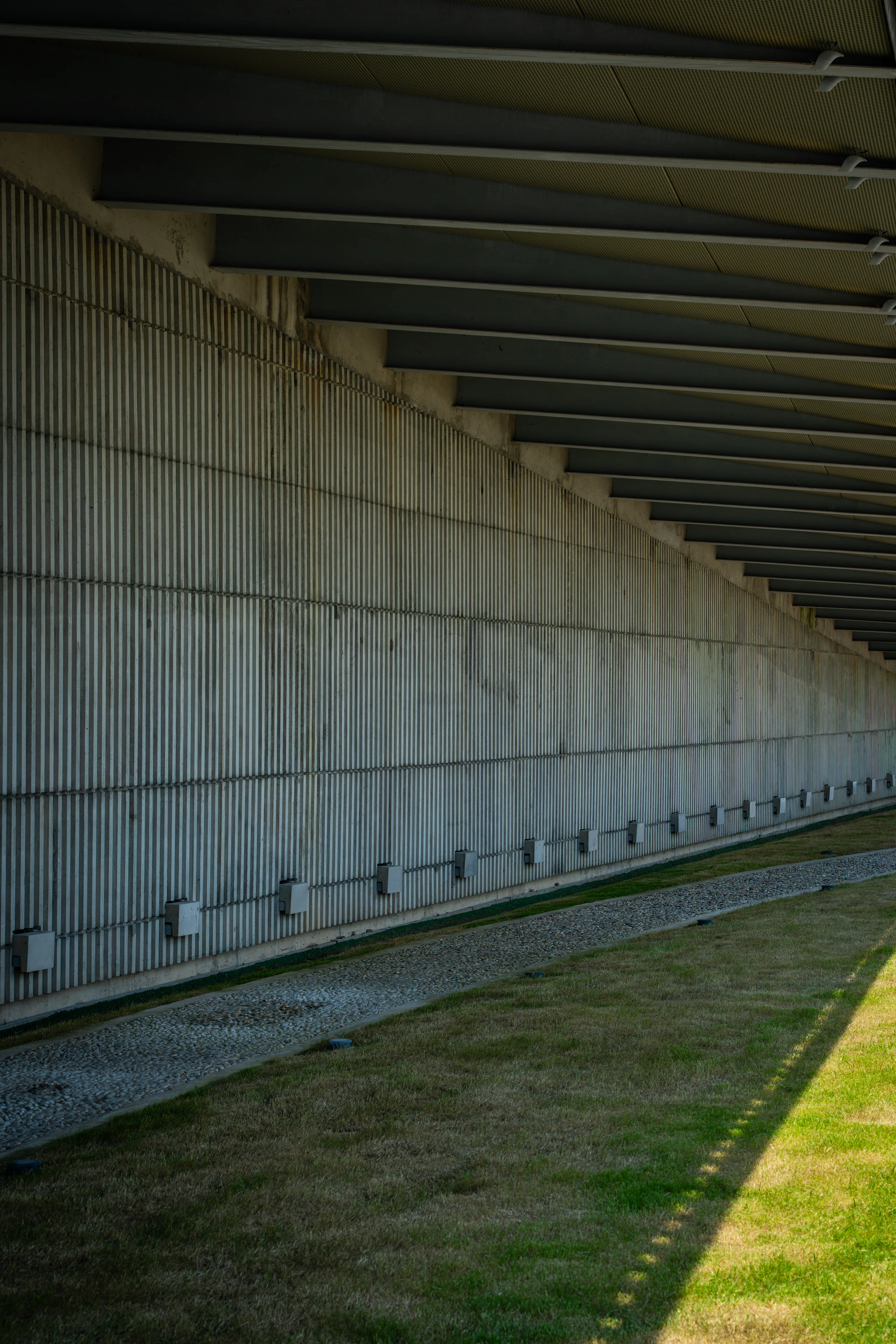 A long board-formed concrete colonnade receding beside a strip of lawn.