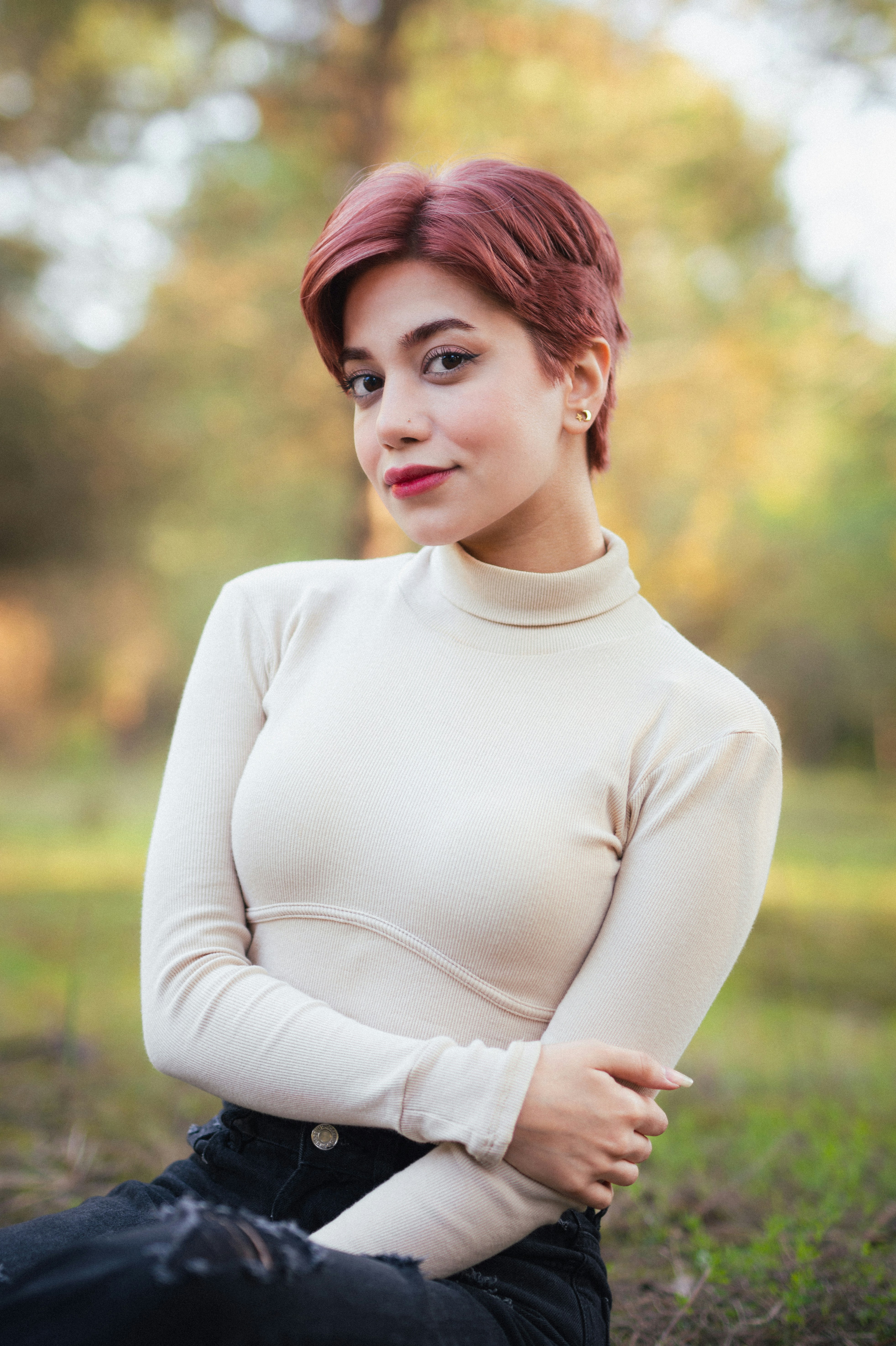 A woman poses outdoors, with red hair.