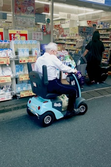 An elderly man rides his scooter by a storefront.