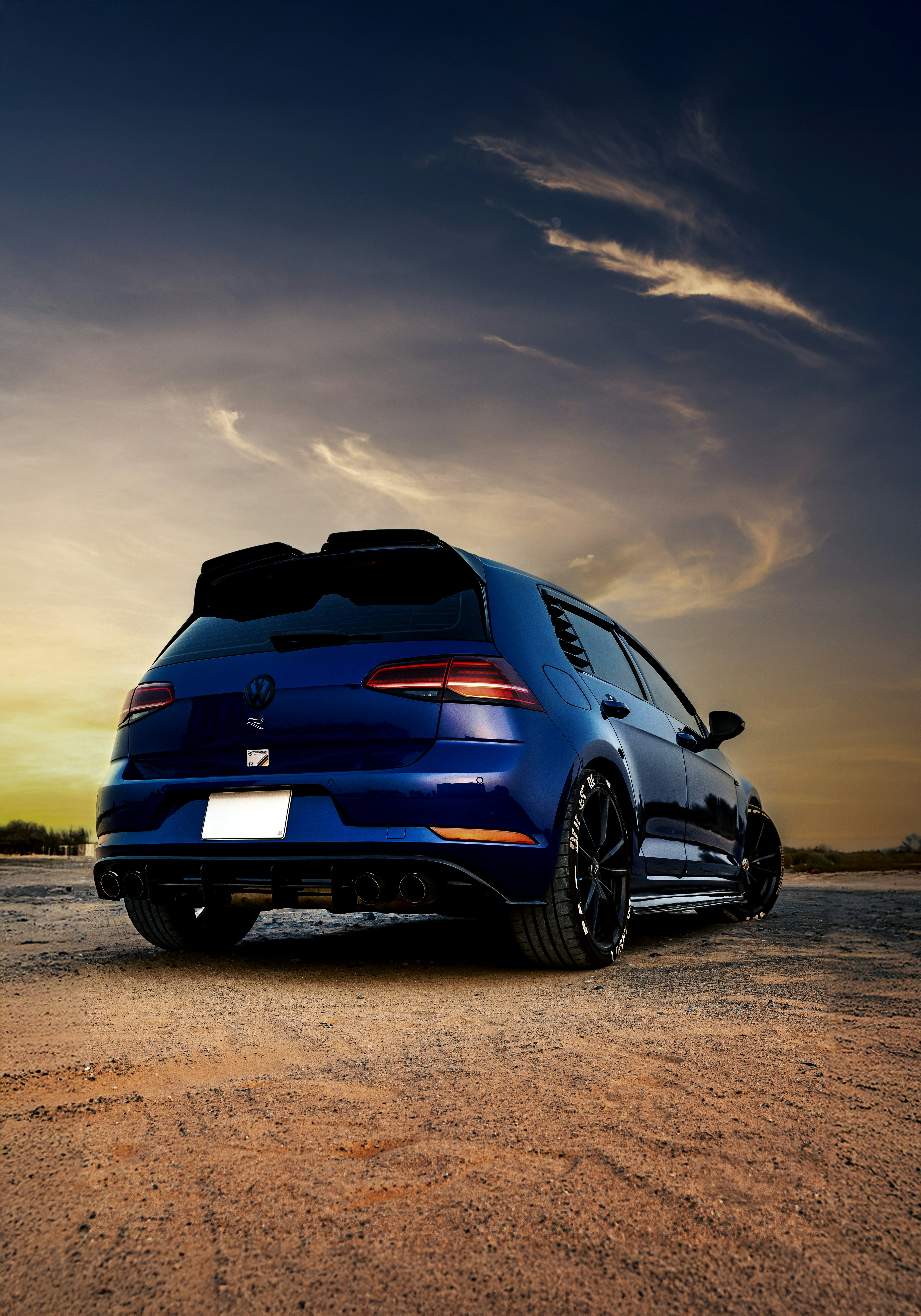 A blue car stands underneath a cloudy sky.