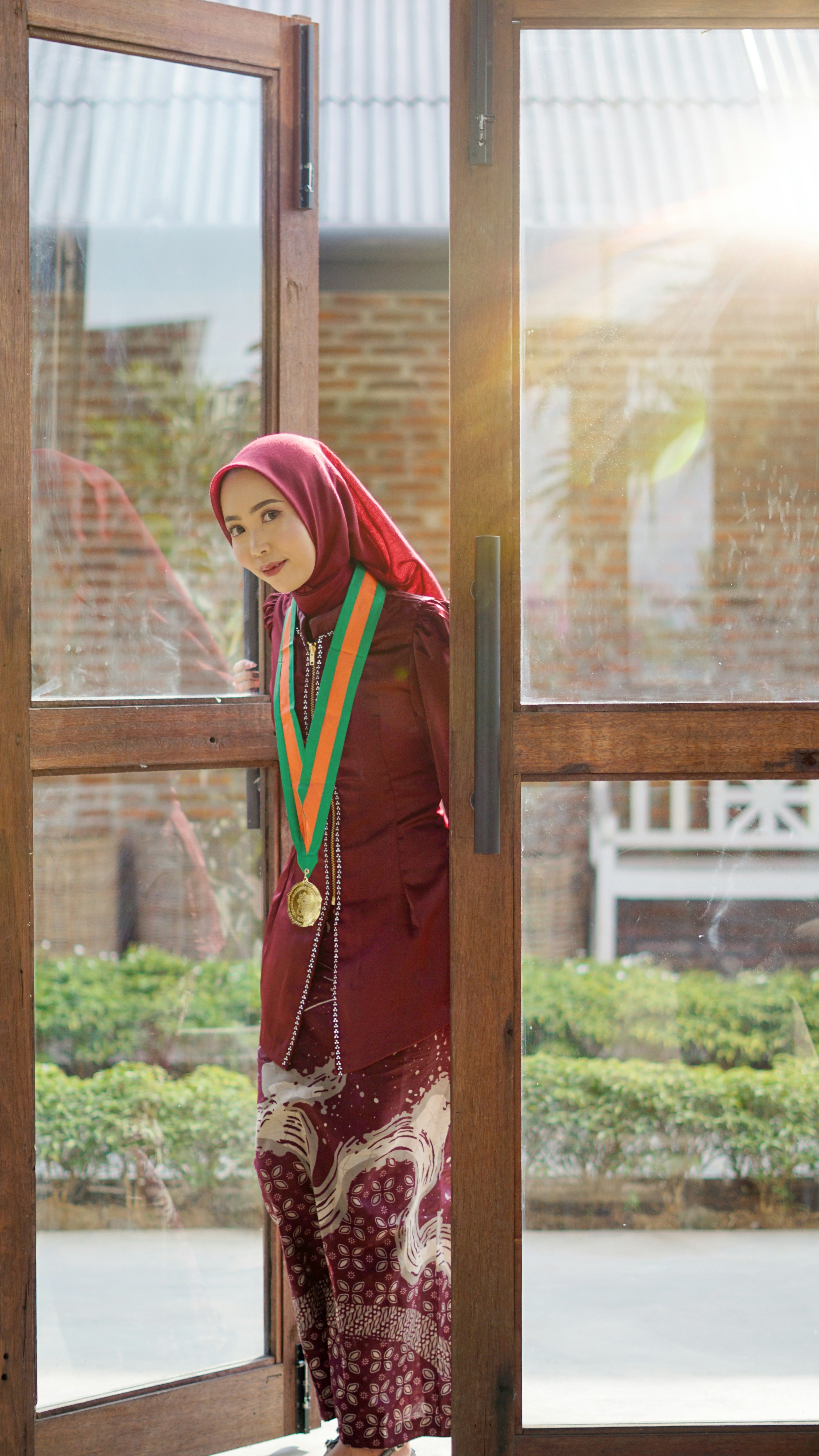 A woman in a hijab and medal peeks through a door.