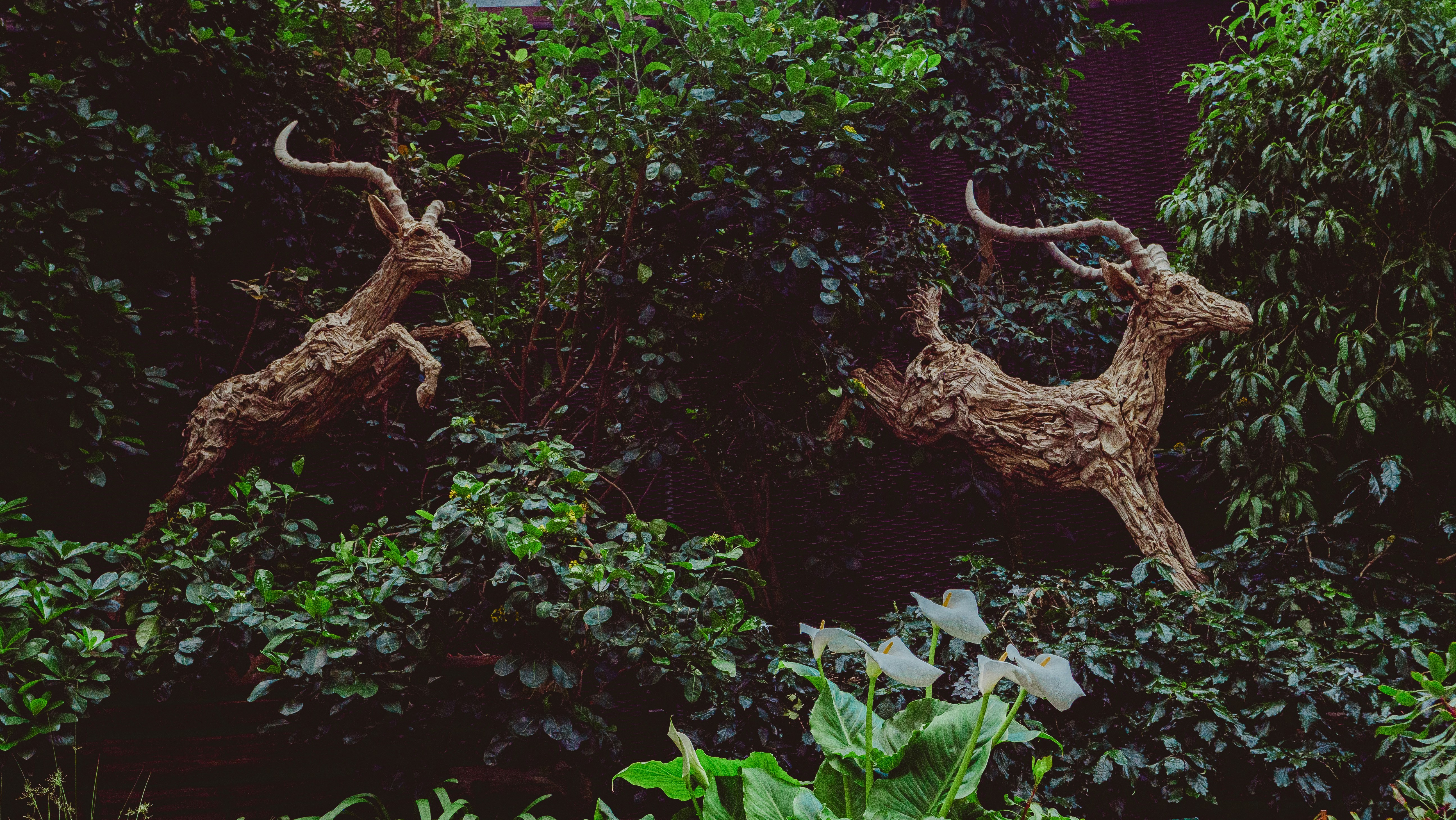 Two sculptures of deer are leaping through foliage.