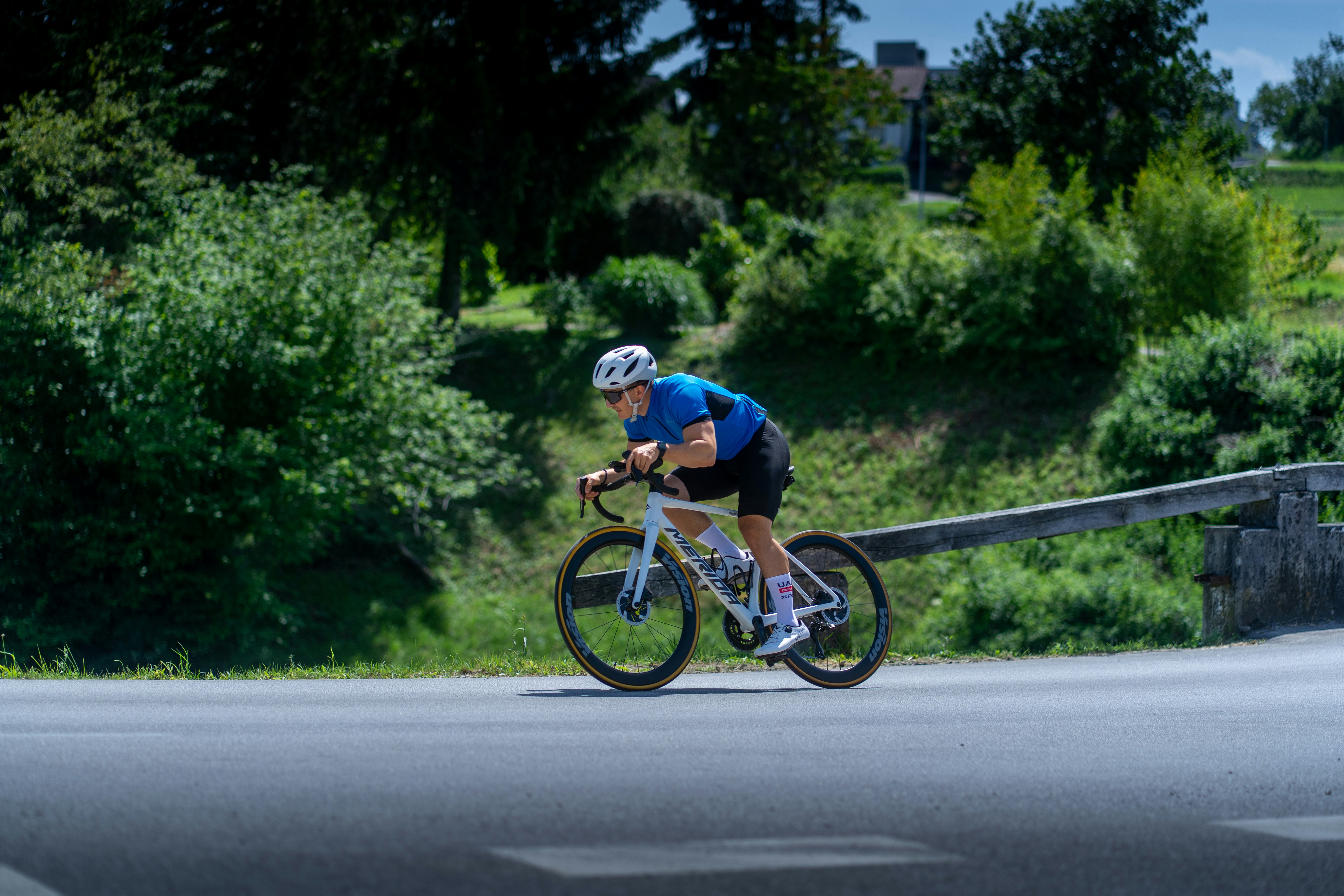 Cyclist races down the road on a sunny day.