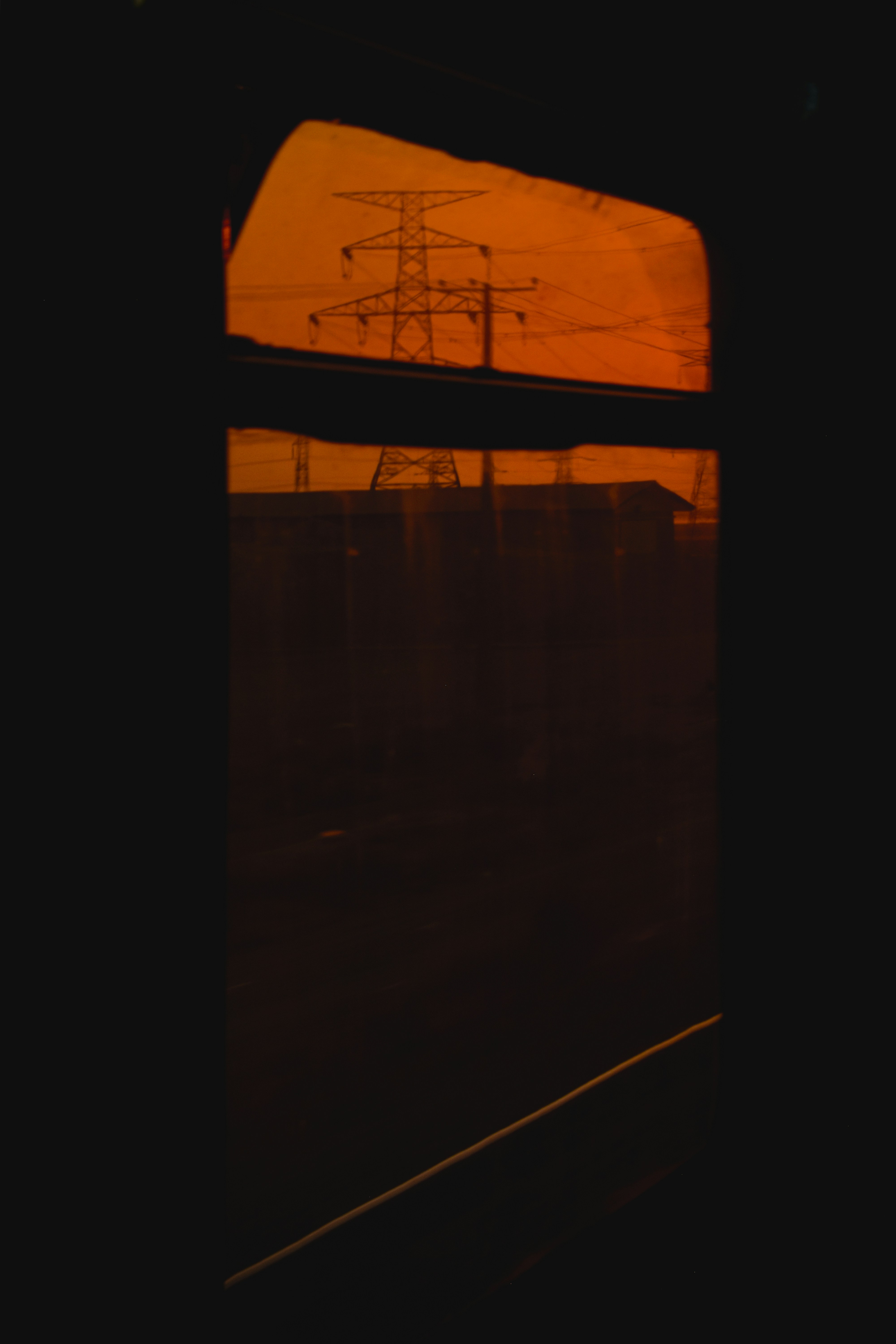 A power tower is silhouetted against an orange sky.