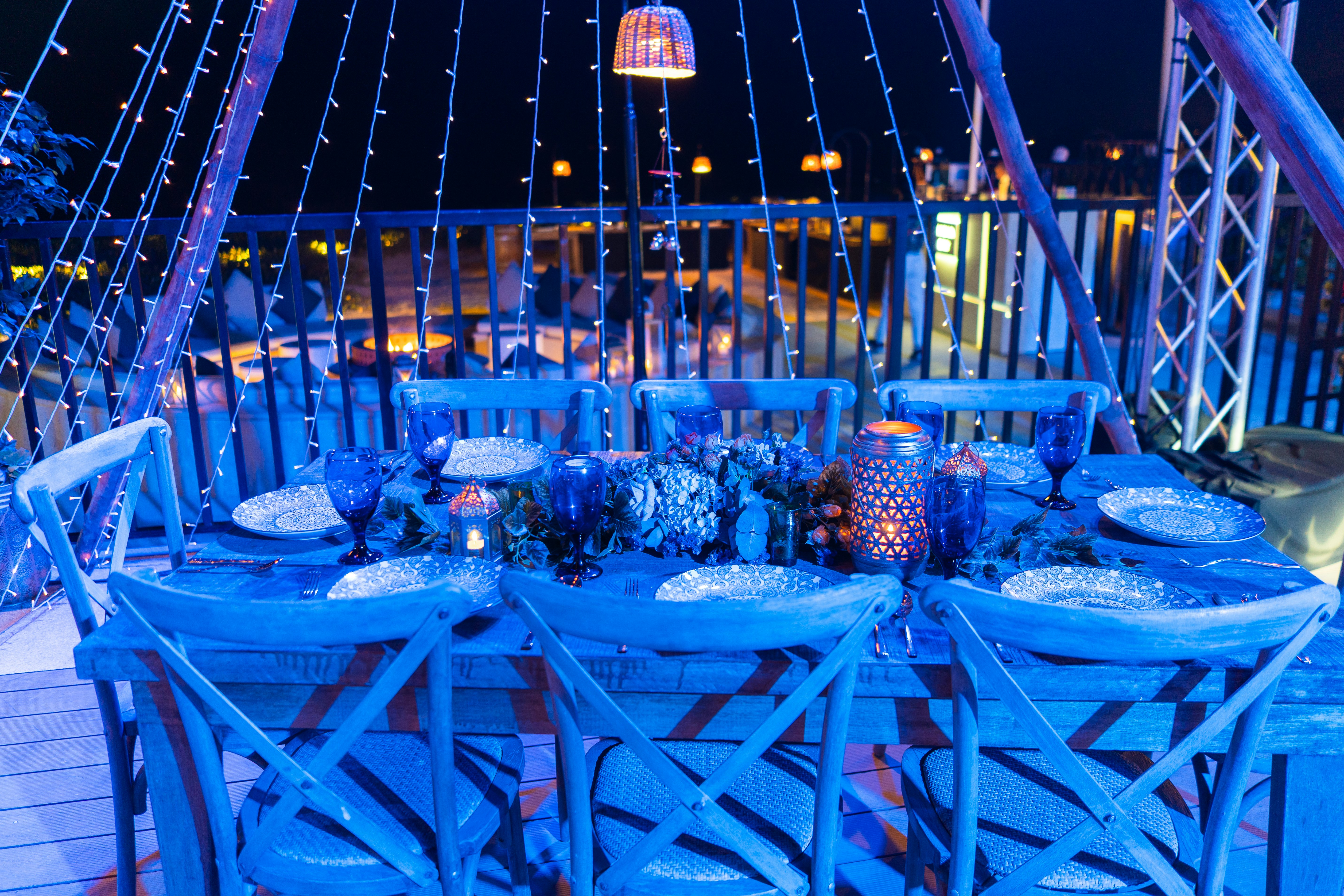 A dinner table is set outdoors with decorative lighting.