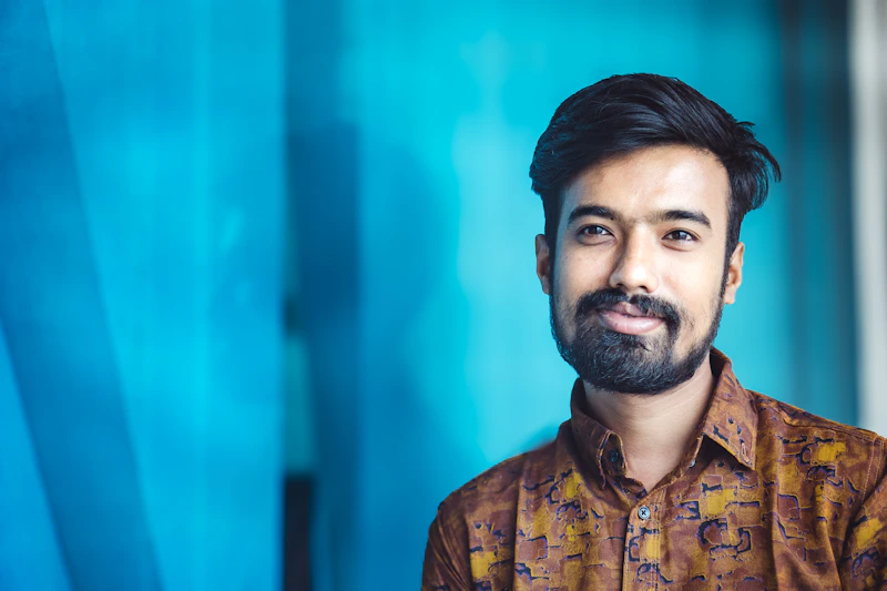 A smiling man poses in front of a blue wall.