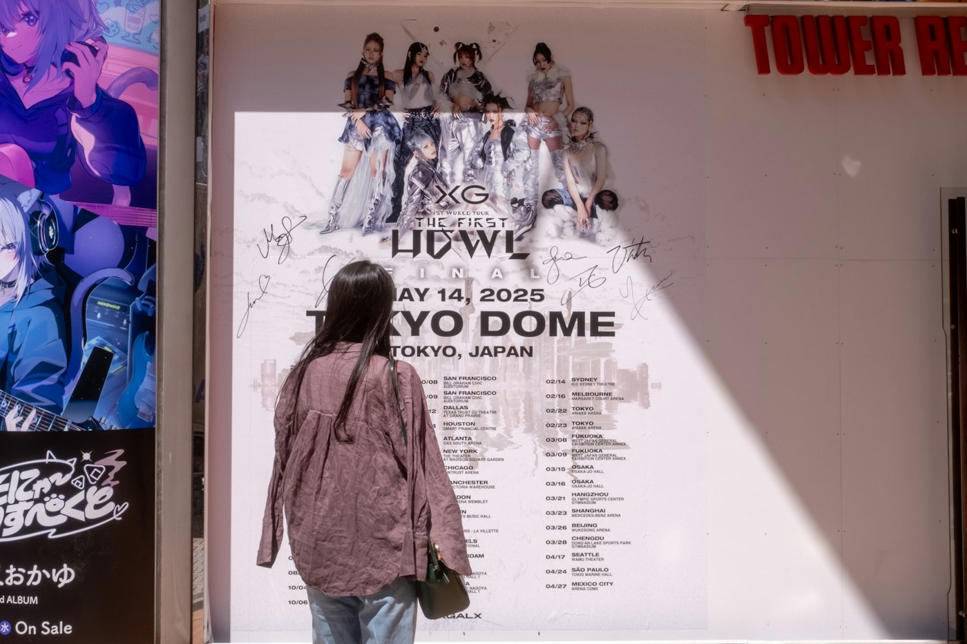 A woman stands in front of a large concert poster in a record store window.