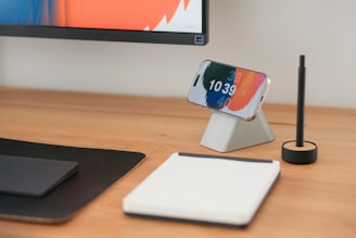 A phone, pad, and pen sit on a wooden desk.